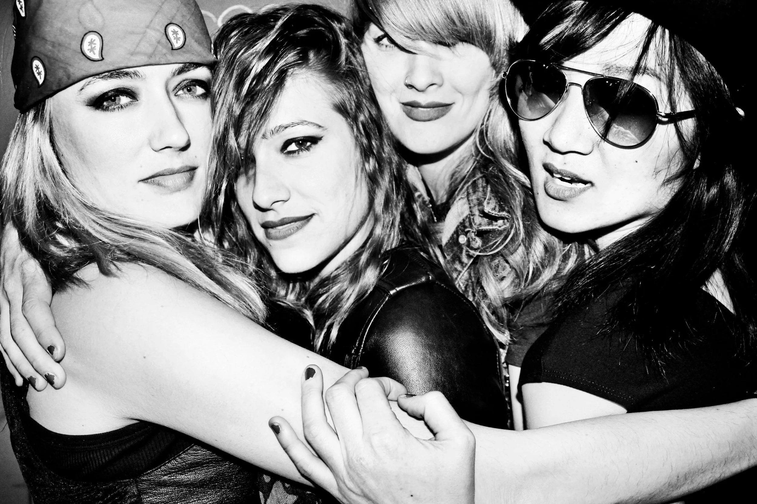 Four women hugging and posing together, all with different hairstyles and expressions, in a black-and-white photo.