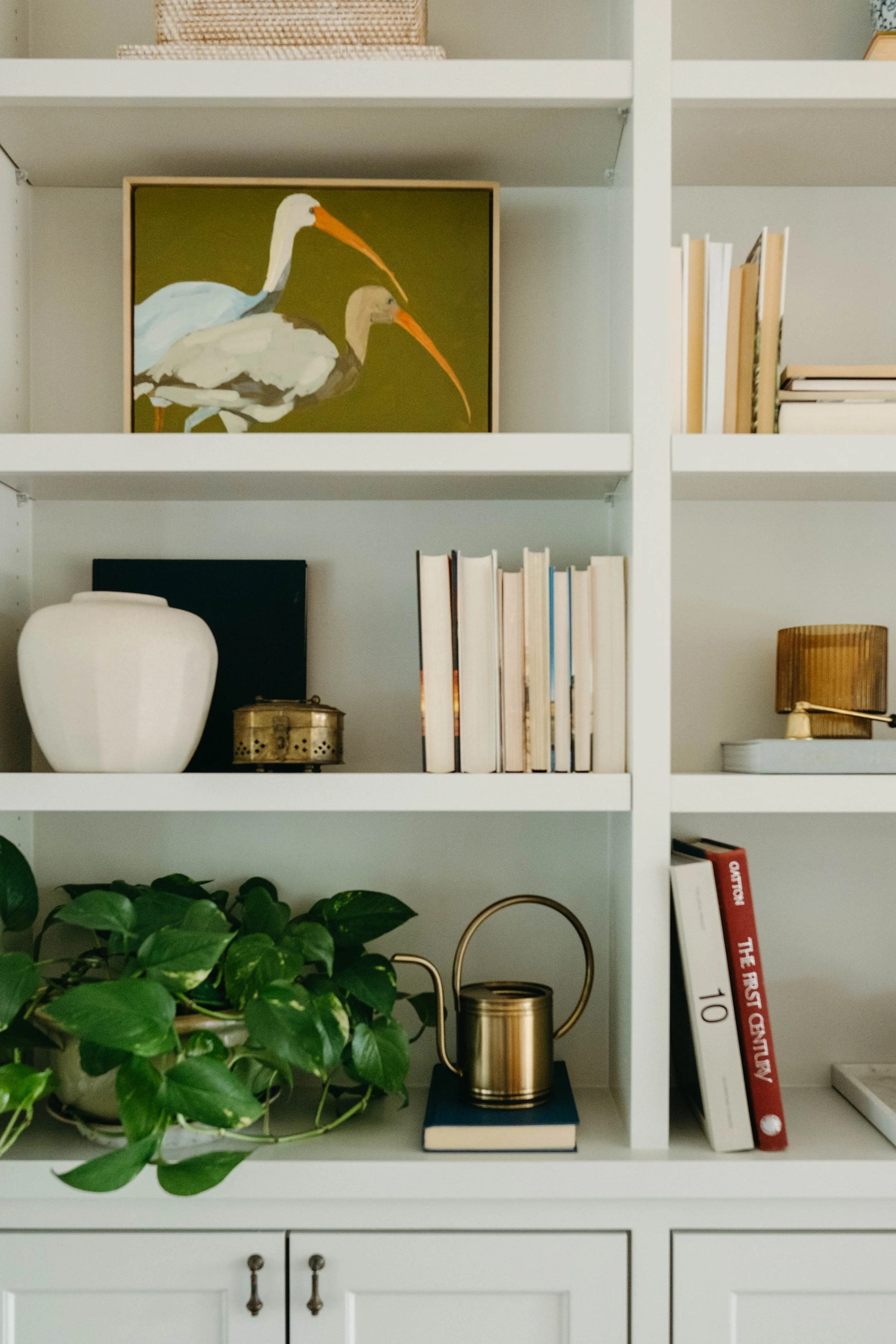 Custom bookshelves with decorative items, books, a plant, and a framed painting of two herons on green background.