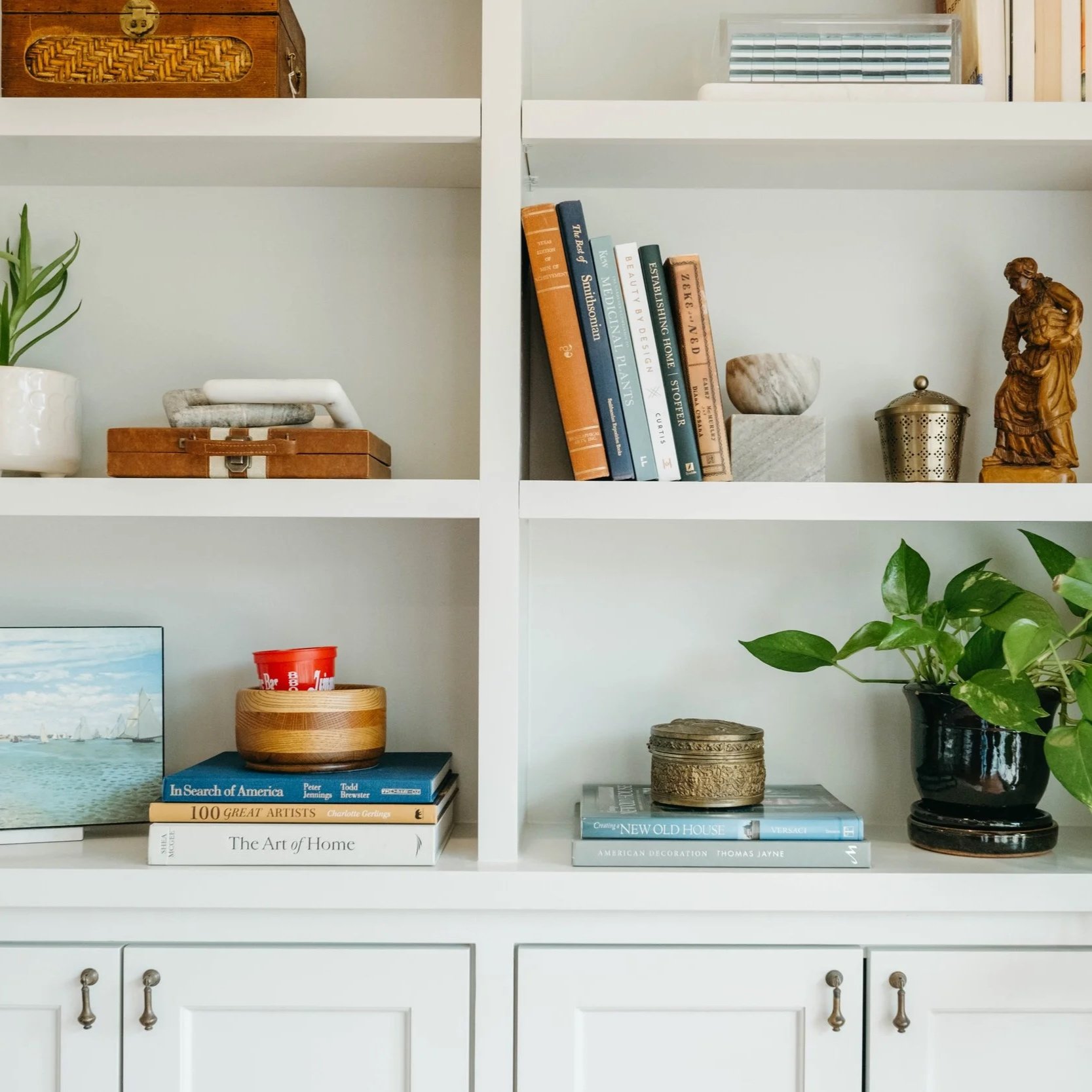 White bookshelf filled with books, plants, decorative objects, and a wooden cabinet.