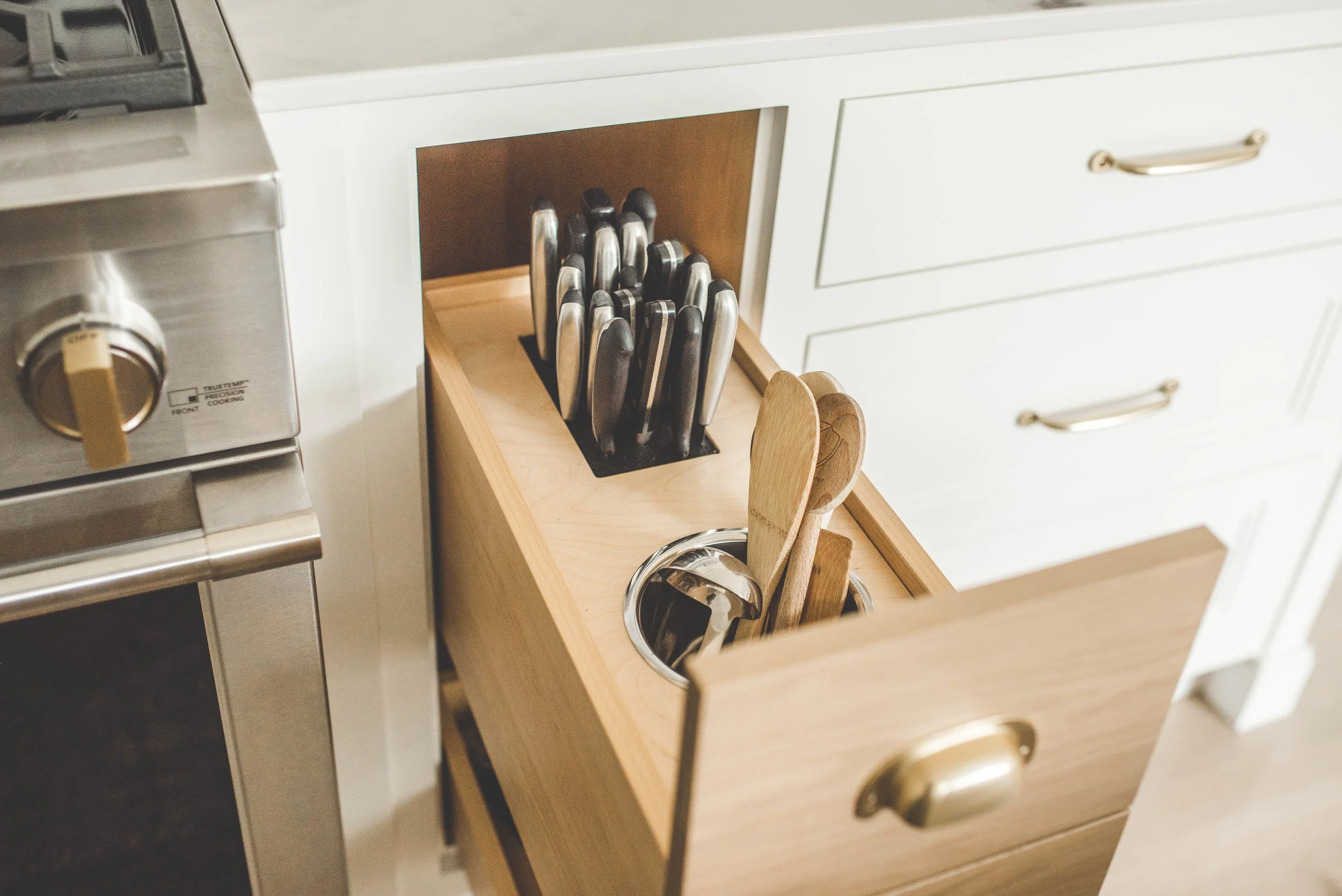 Open kitchen drawer with wooden utensils and knife set inside.