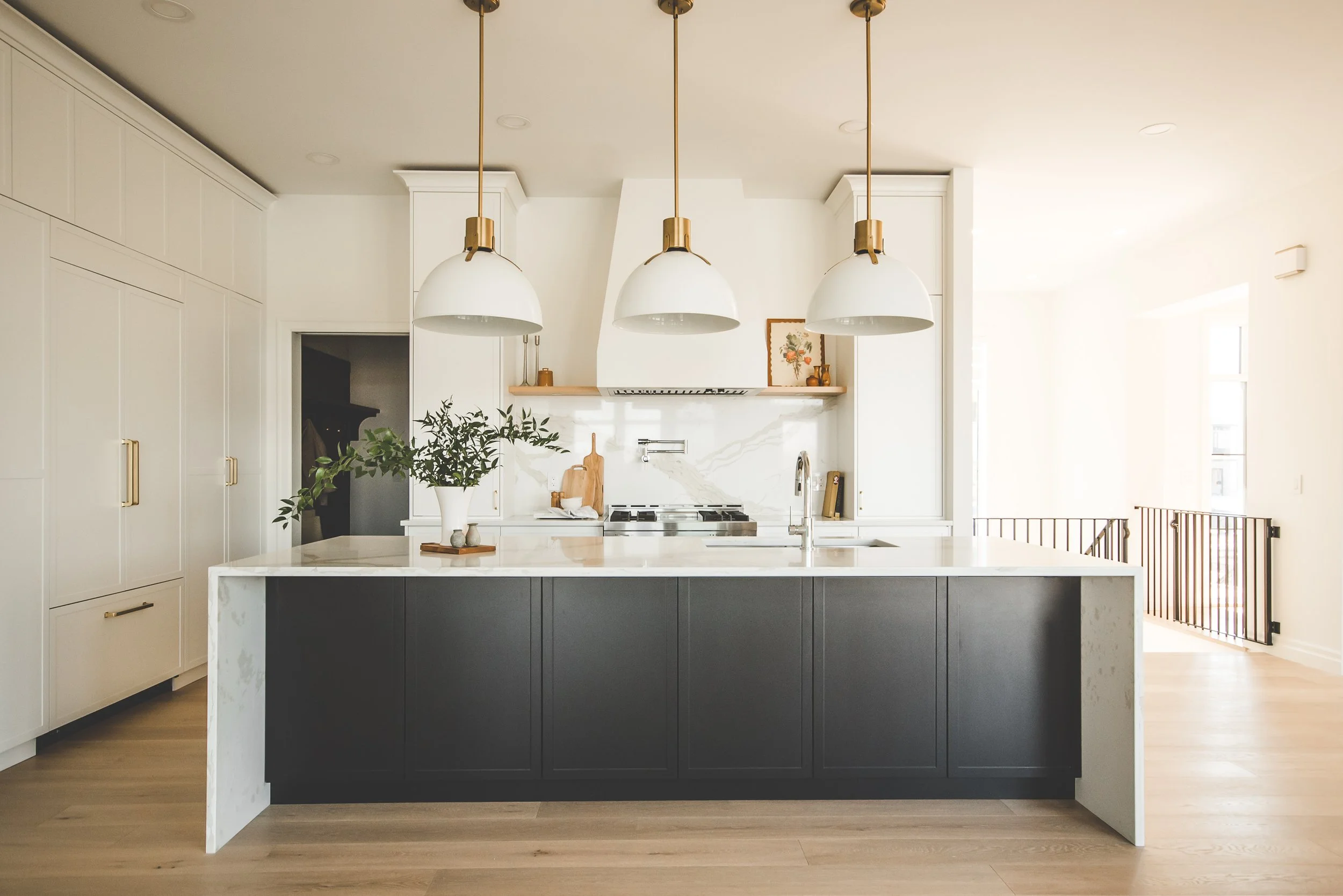 Modern kitchen with black island, white cabinets, gold hardware, pendant lights, and a marble backsplash.