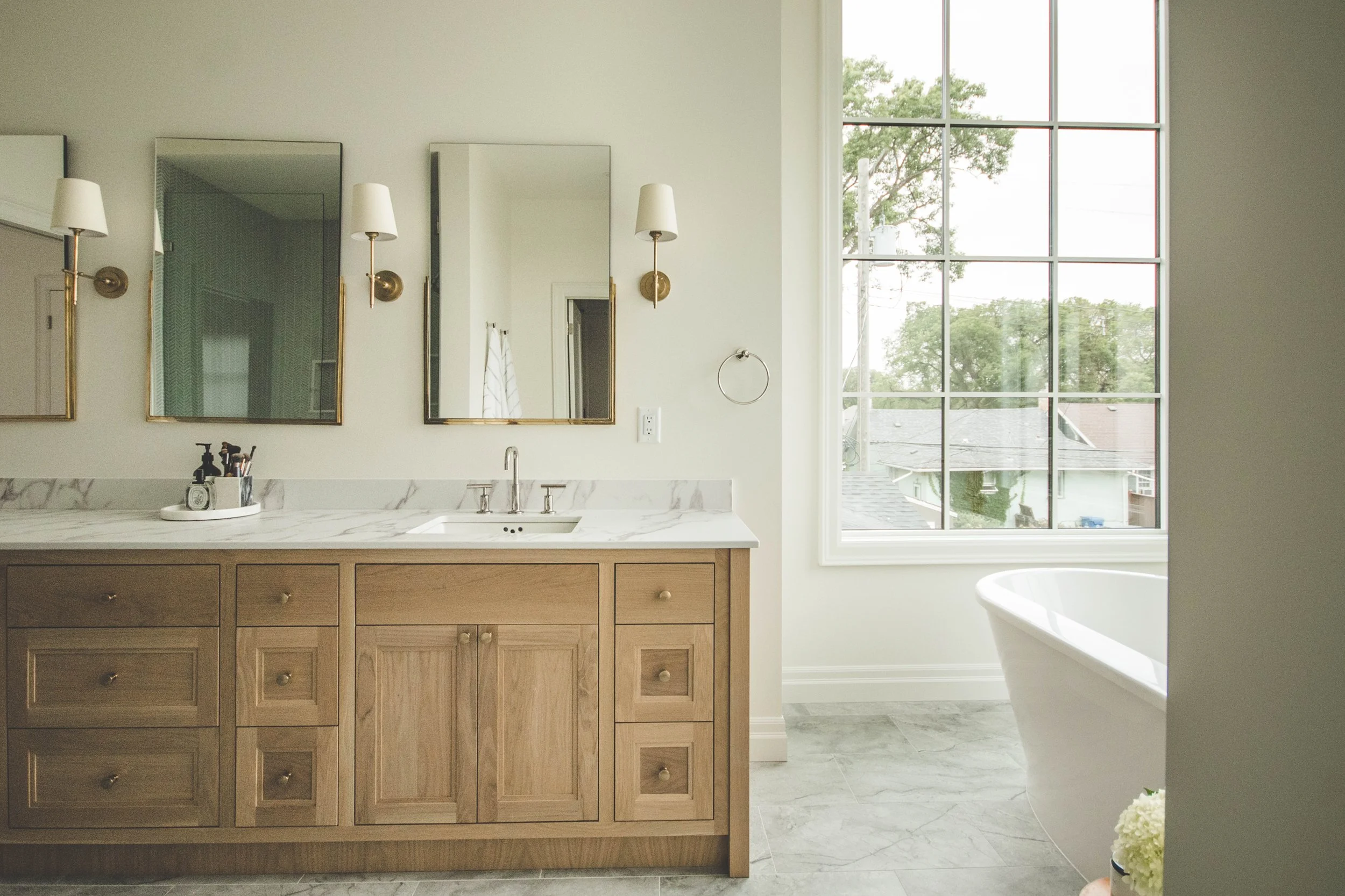 Modern bathroom with a large window, wooden vanity with marble countertop, and a bathtub.