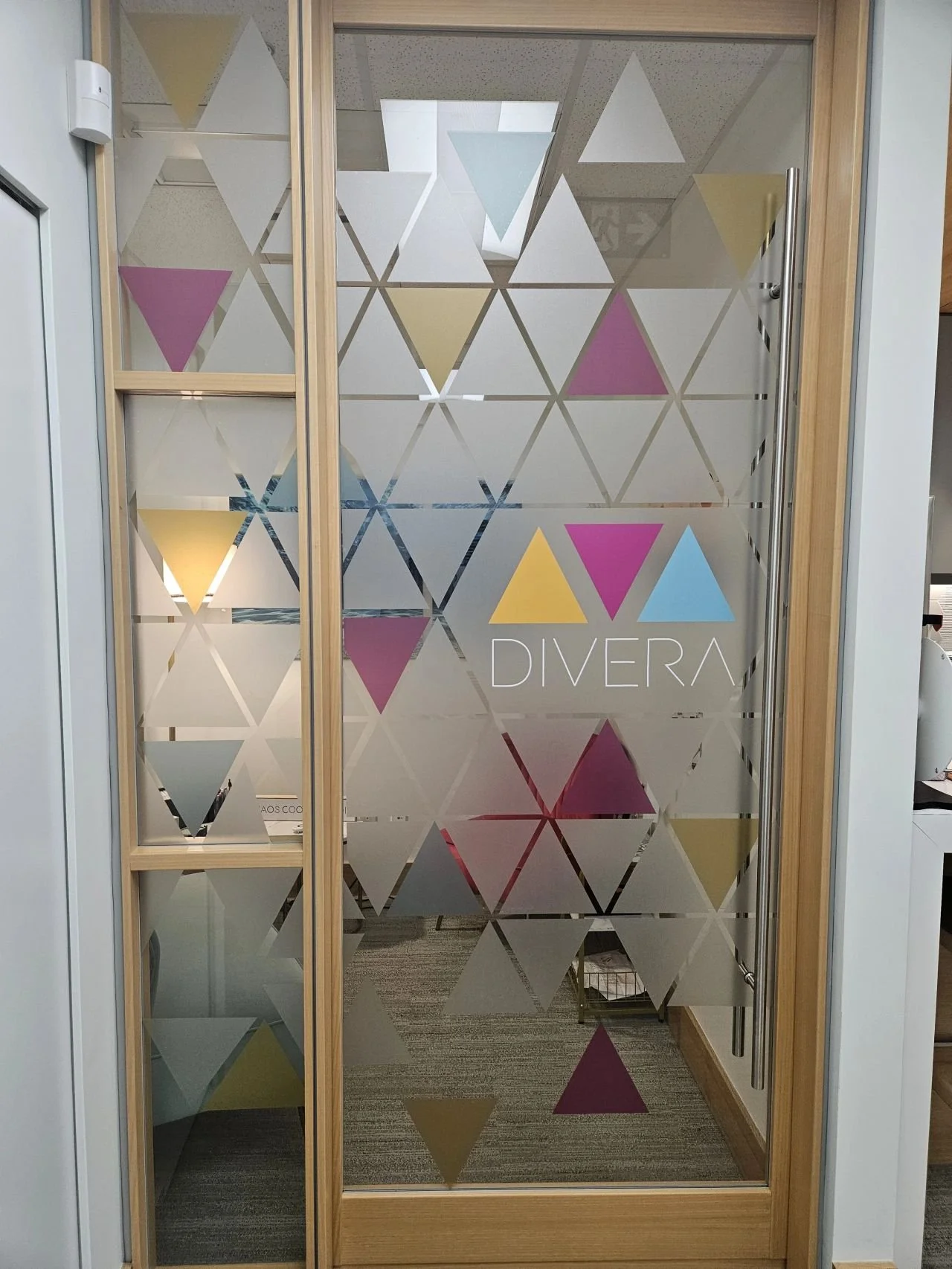 Divera Vancouver Vanessa Luv Founder Glass door with geometric triangle patterns in purple, yellow, blue, and white, and the word "DIVERA" written on it.