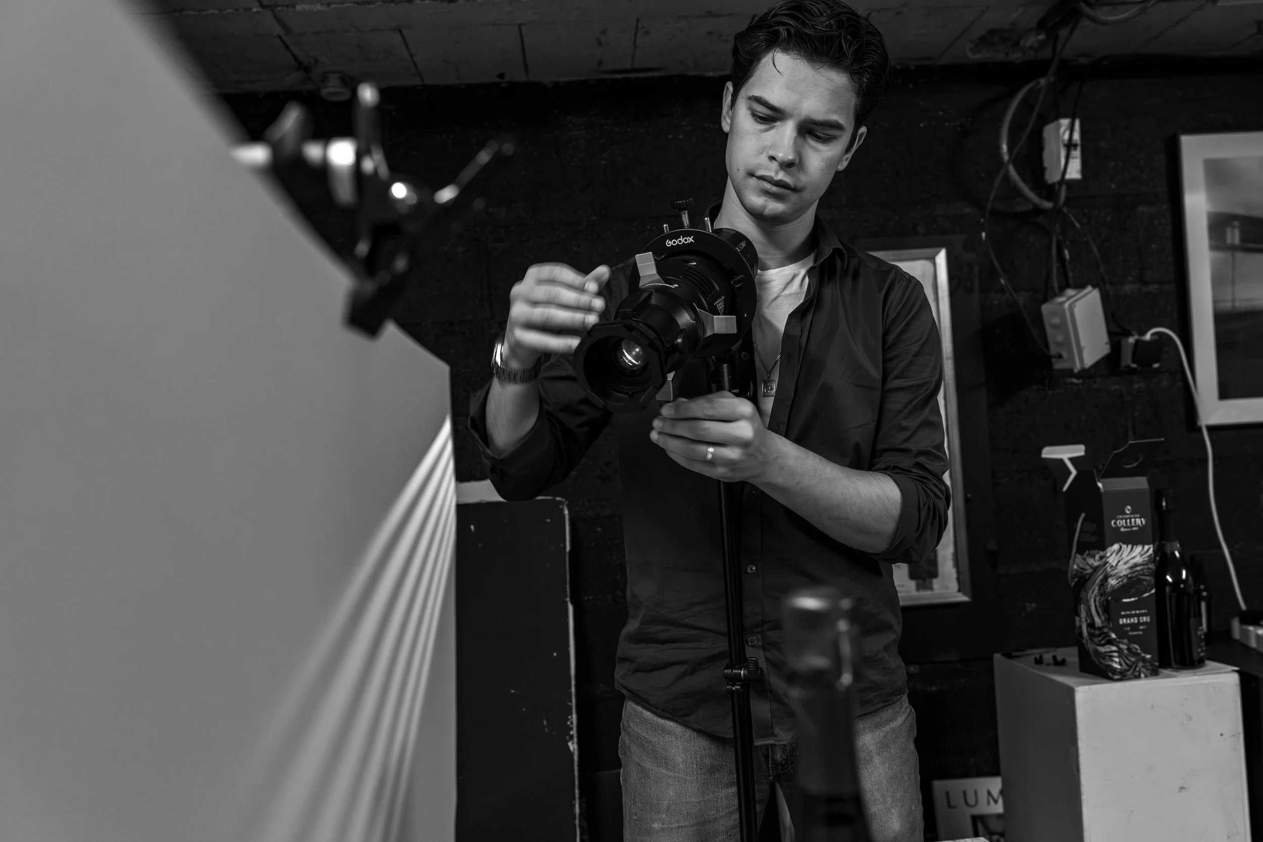Théo WALLYN, TheWallPhoto réglant une caméra de film sur un trepied dans un studio photo, en noir et blanc.