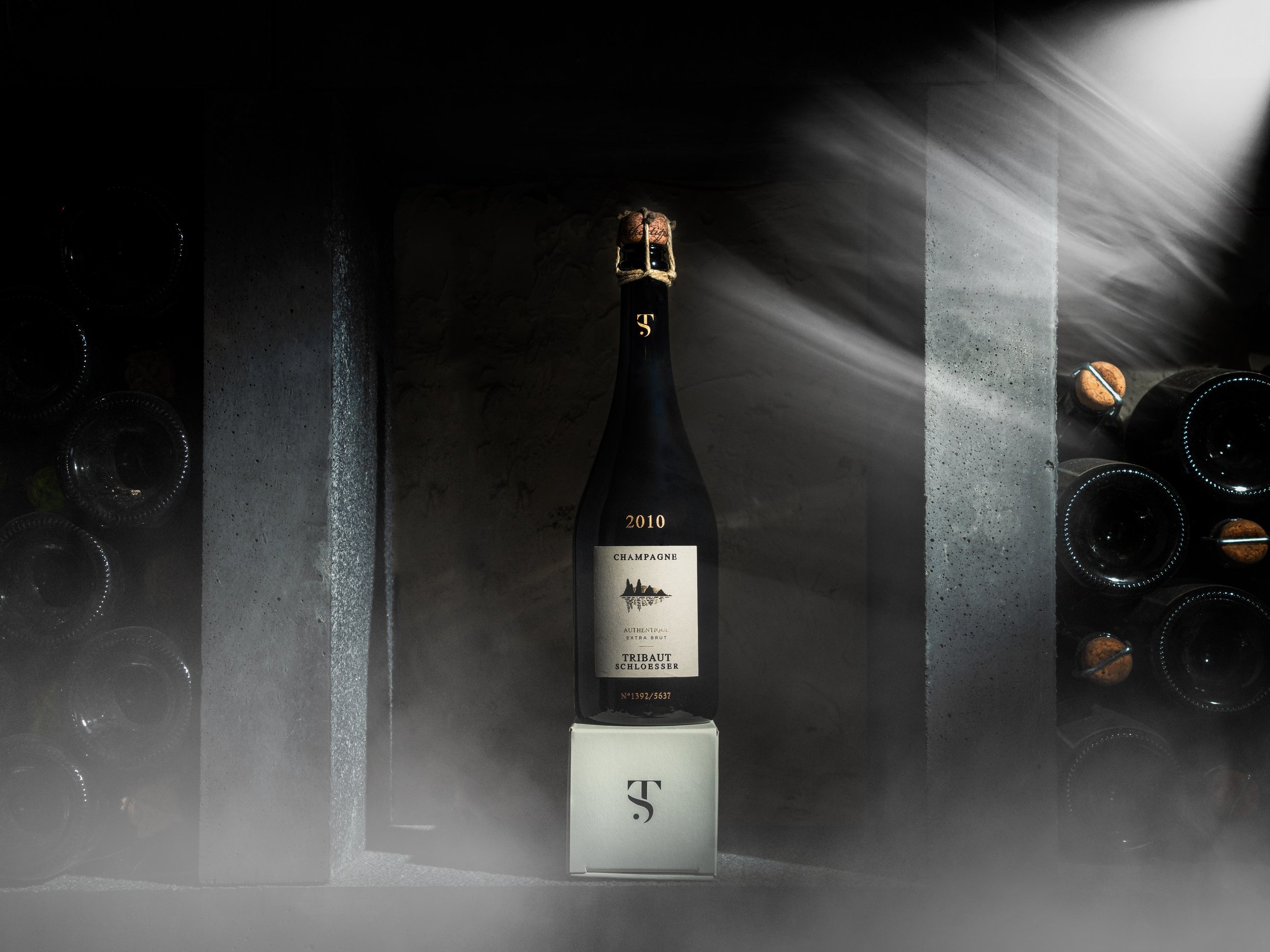 Bouteille de champagne dans une cave, entourée de bouteilles couchées allongées, avec lumière diffuse et brume artistique. Photo prise par Théo WALLYN, TheWallPhoto.