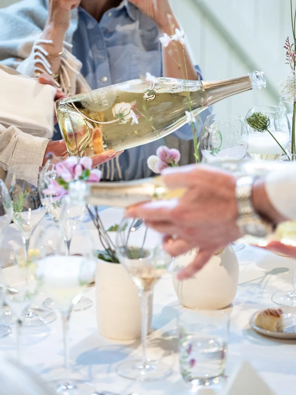 Gens versant du champagne Perrier Jouet dans un verre belle époque lors d'un repas élégant avec des fleurs sur la table. Photo prise par Théo WALLYN, TheWallPhoto.