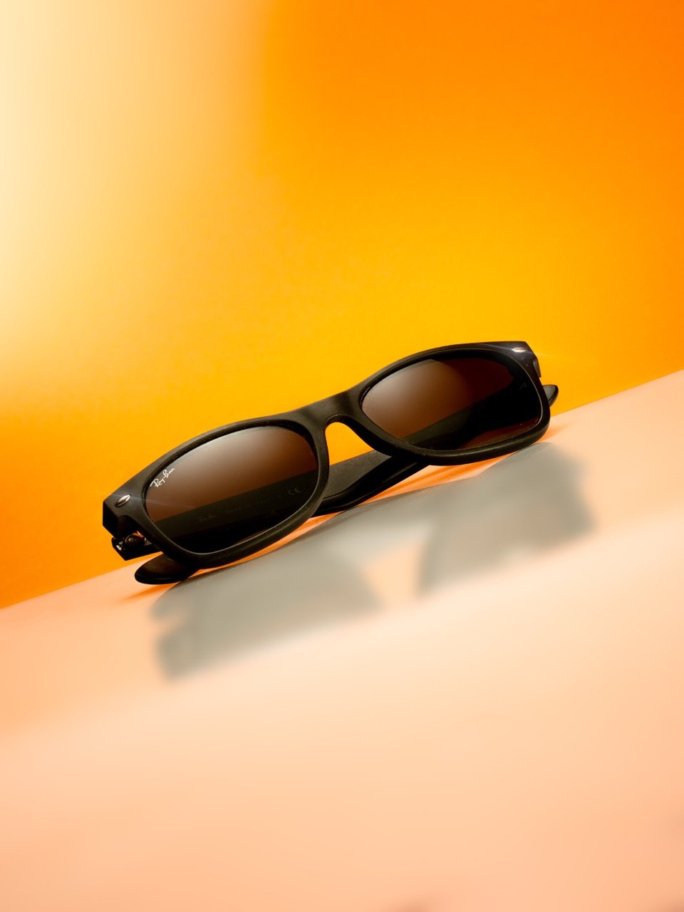 Lunettes de soleil noires Ray-Ban posées sur une surface claire, avec un fond orange.