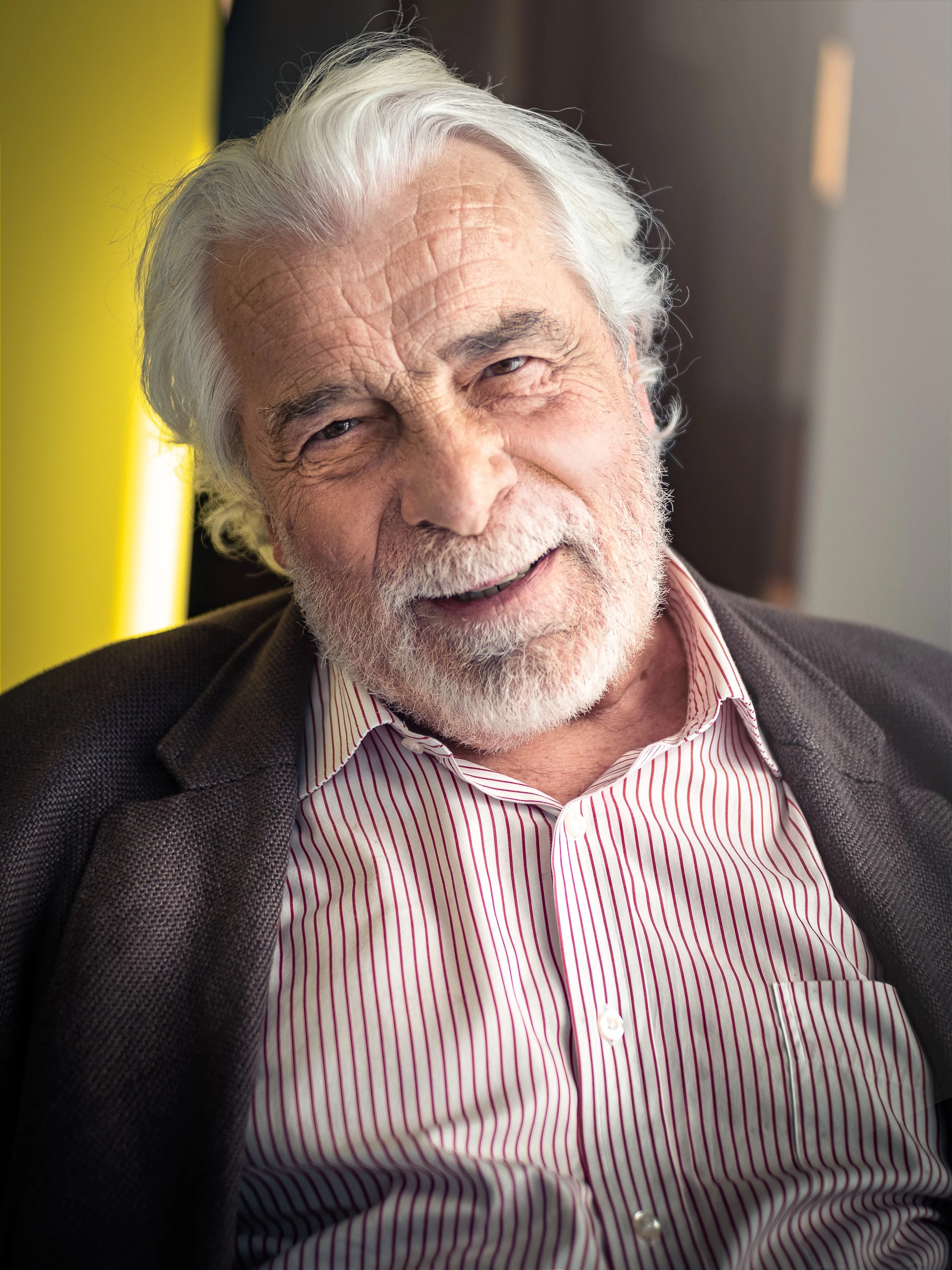 Jacques Weber souriant, avec des cheveux gris et une barbe blanche, portant une chemise à rayures et une veste noire, lors du festival Reims Polar. Photo prise par Théo WALLYN, TheWallPhoto.