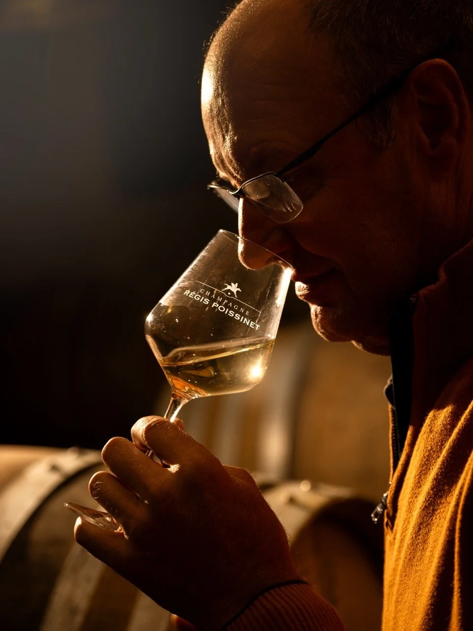 Un homme portant des lunettes sentant un verre de champagne dans une cave ou un chai. champagne Poissinet. Photo prise par Théo WALLYN, TheWallPhoto.