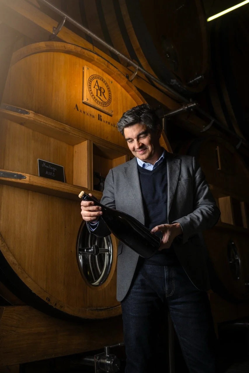 Le président de la maison de champagne AR Lenoble souriant examine une bouteille de champagne dans une cave,  devant ses foudres en bois. Photo prise par Théo WALLYN, TheWallPhoto.