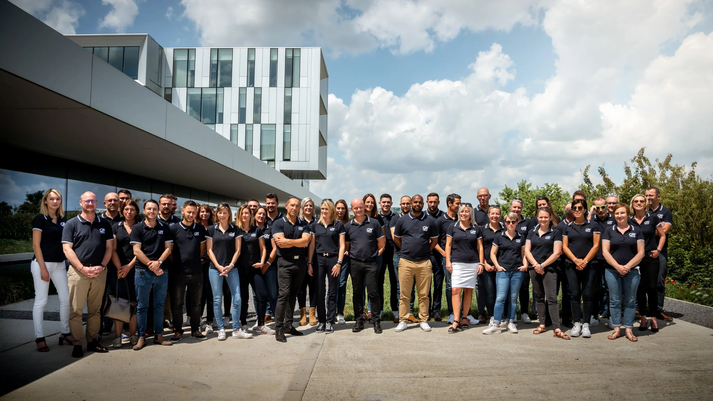 Groupe de personnes portant des polos noirs avec le logo d'une entreprise, devant un bâtiment moderne en journée ensoleillée. Groupe crédit agricole village by CA de Bezannes Photo prise par Théo WALLYN, TheWallPhoto.