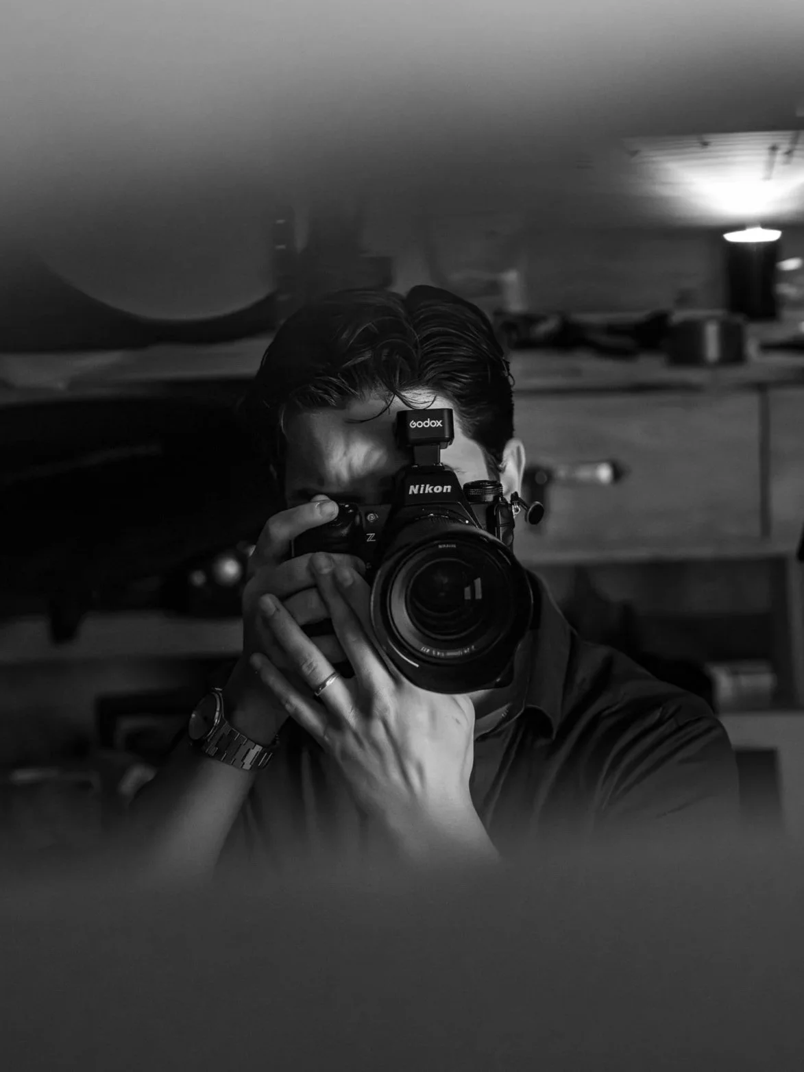 Théo Wallyn, TheWallphoto prenant une photo de lui-même avec un appareil photo Nikon, reflet dans un miroir, fond flou, en noir et blanc.