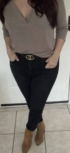 A woman wearing a beige V-neck top, black jeans with a Gucci belt, and tan high-heeled boots.