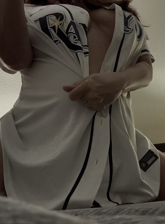 A person in white sportswear with black and gold design details, lifting their shirt to reveal their chest and stomach area.