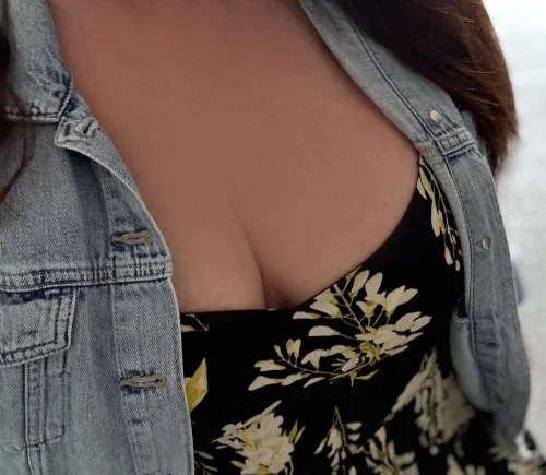 Close-up of a woman wearing a denim jacket over a floral dress with a deep neckline.