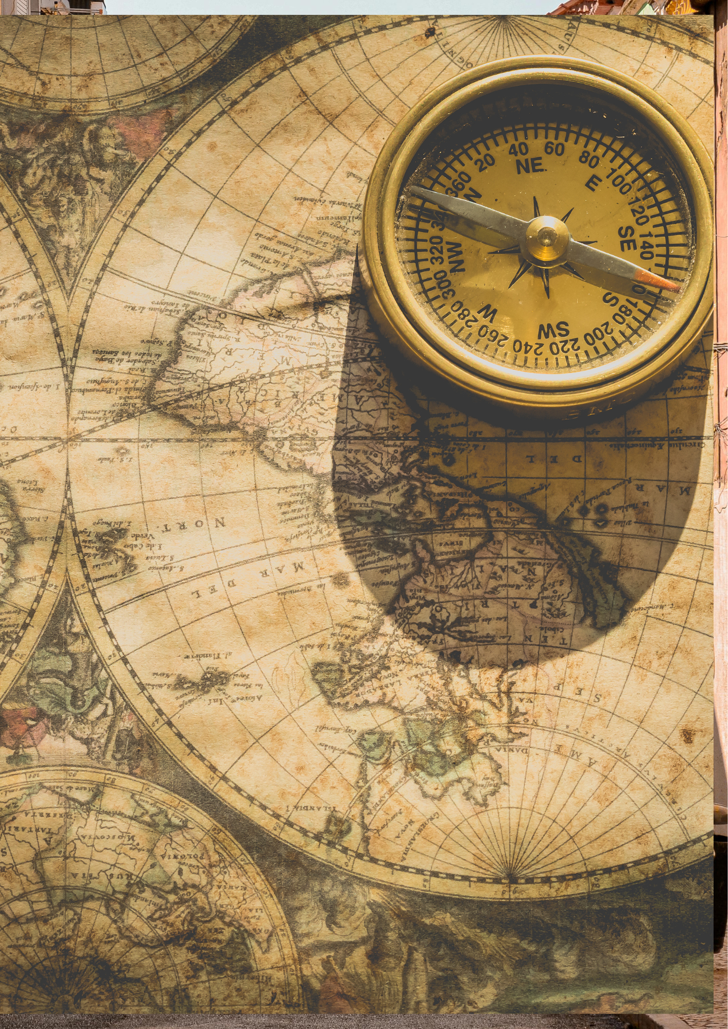 An antique world map with a yellow compass resting on top, casting a shadow. The map features old-style illustrations and longitude and latitude lines.