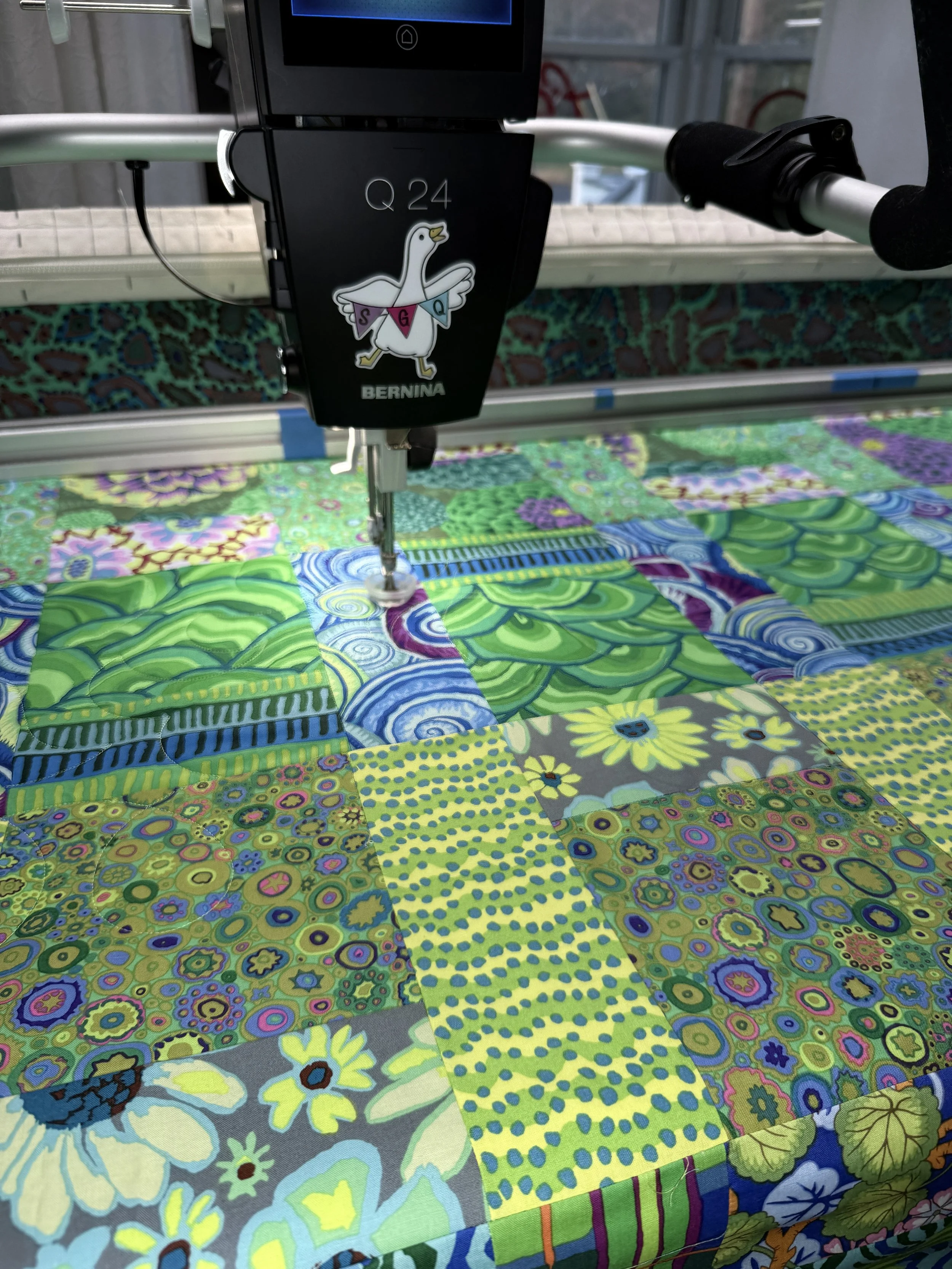 A quilt with colorful floral and geometric patterns being sewn by a sewing machine.