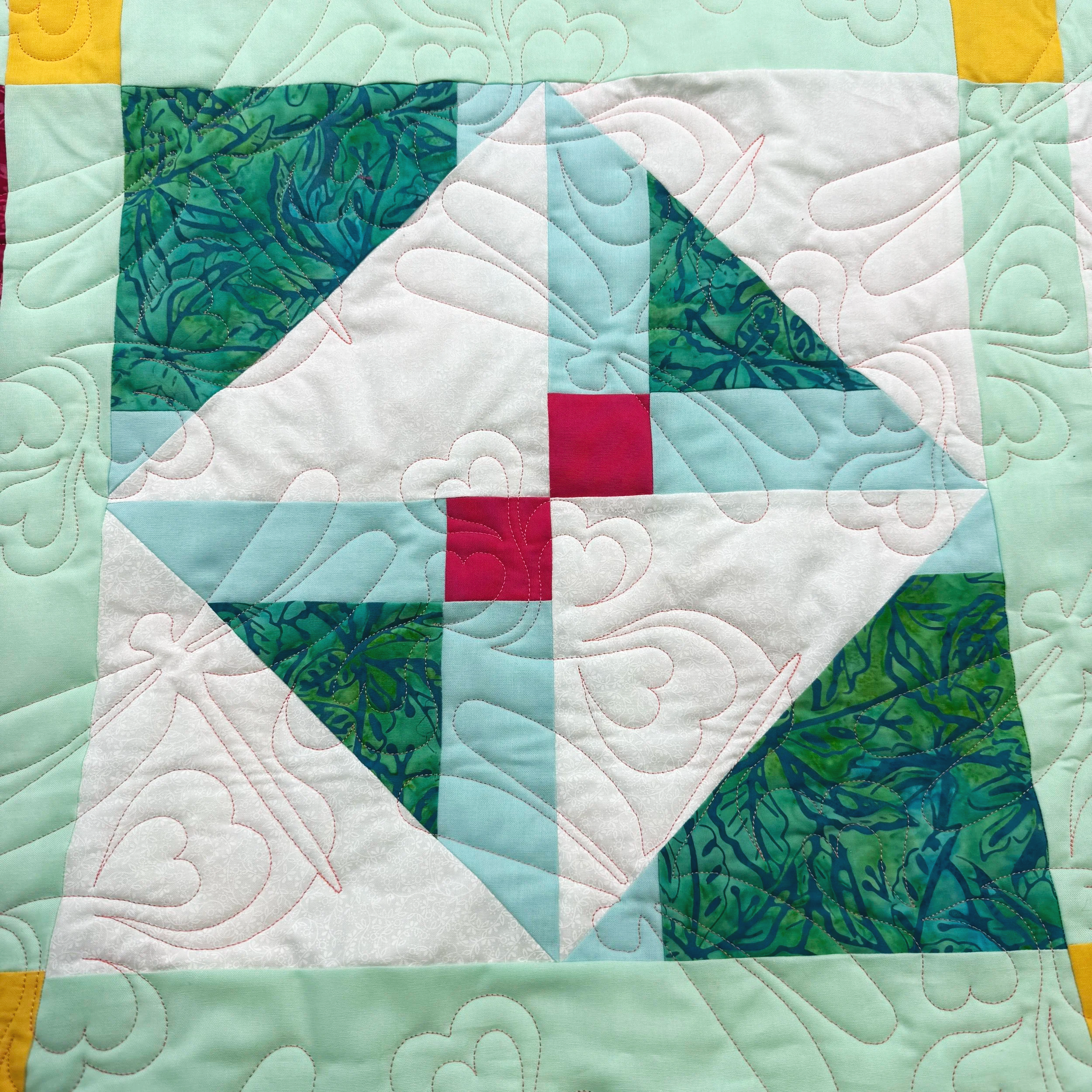 A patchwork quilt with various pastel-colored fabric pieces, including mint green, white, blue, pink, and yellow. Intricate quilting patterns of swirling and curved lines are visible on the fabric.