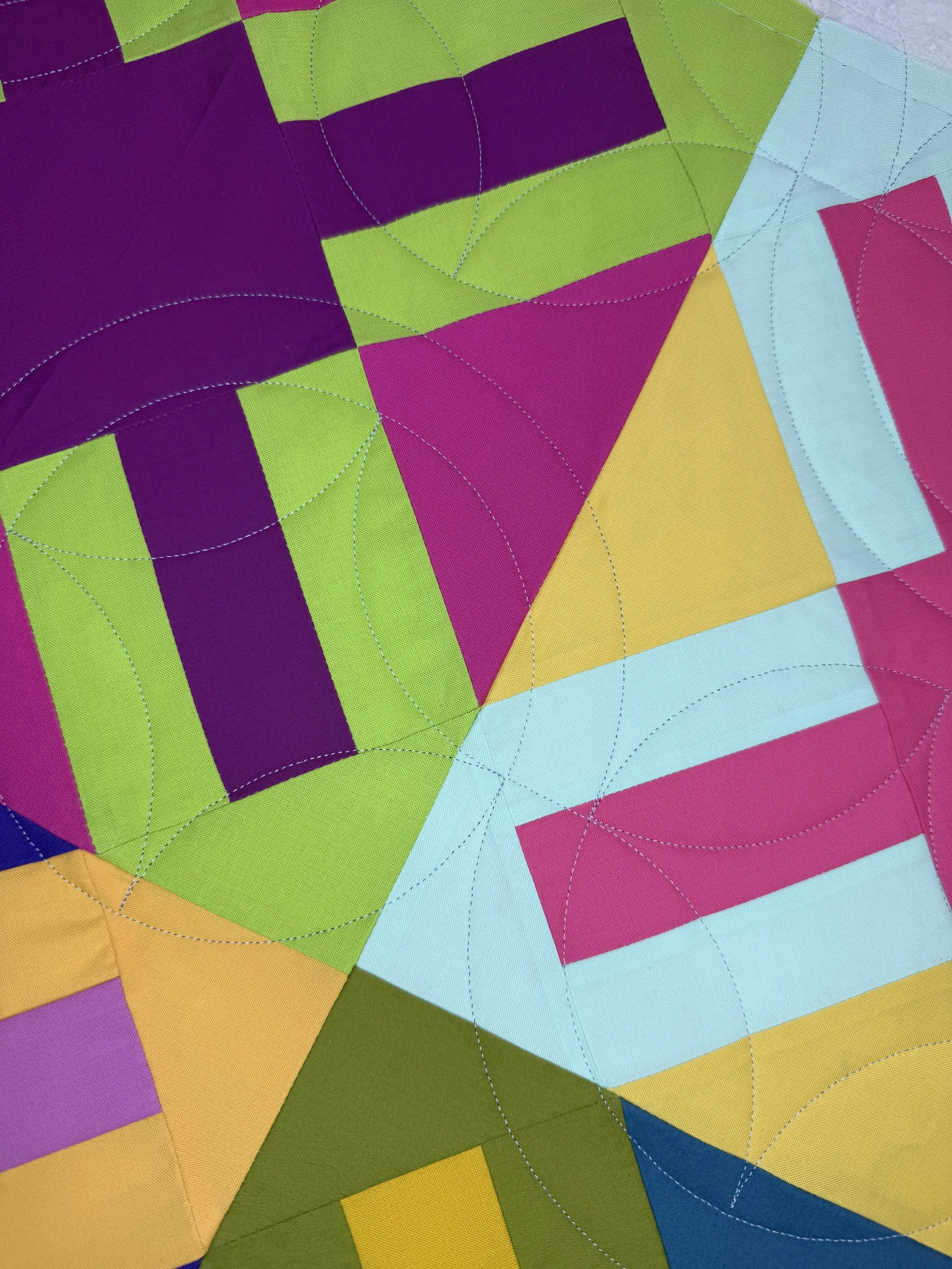 Close-up of a colorful quilt or textile with geometric shapes and stitched circular patterns, featuring colors like purple, green, pink, yellow, blue, and orange.