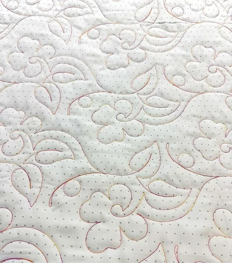 Close-up of white quilted fabric with floral and leaf patterns outlined in red and gold threads.