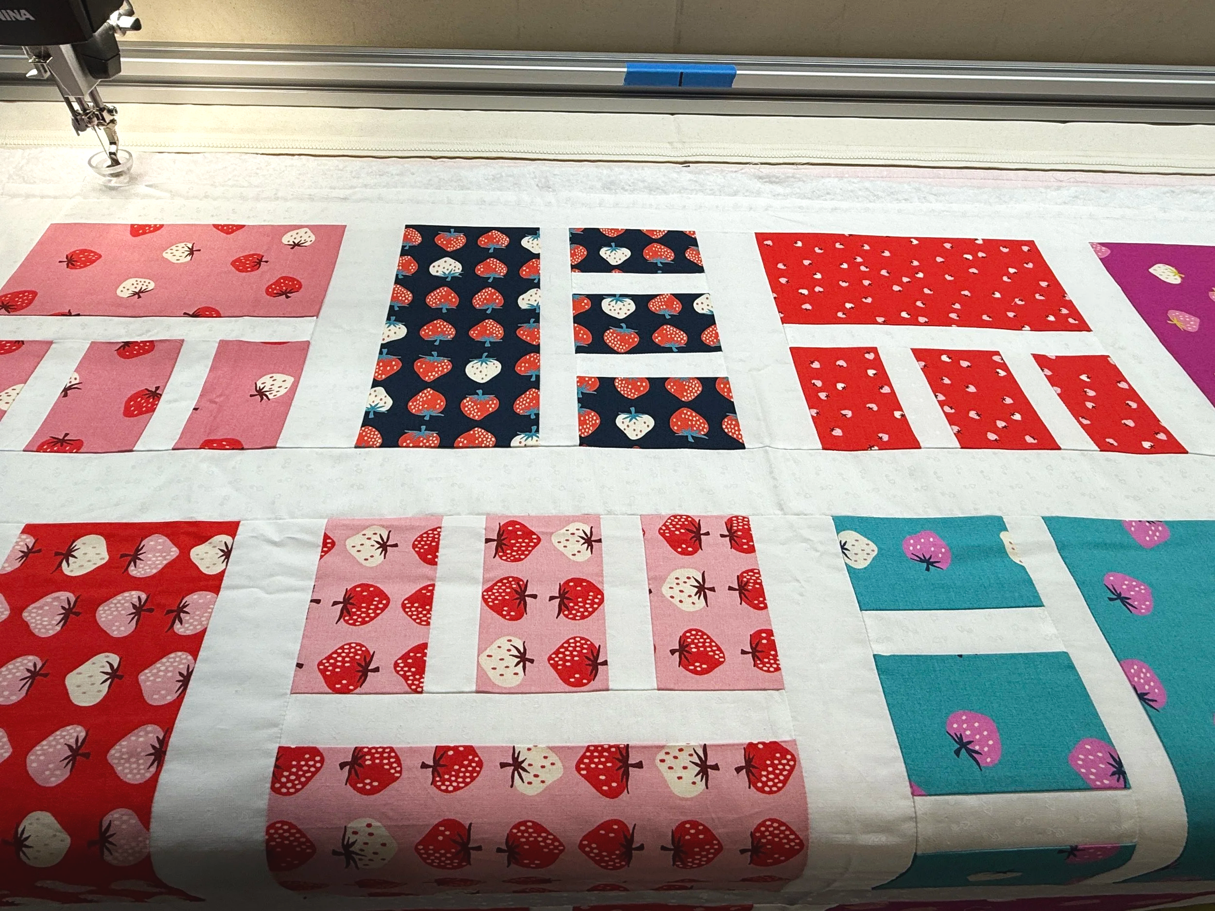 Various fabric pieces with strawberry and fruit patterns laid out on a cutting table for quilting or sewing.