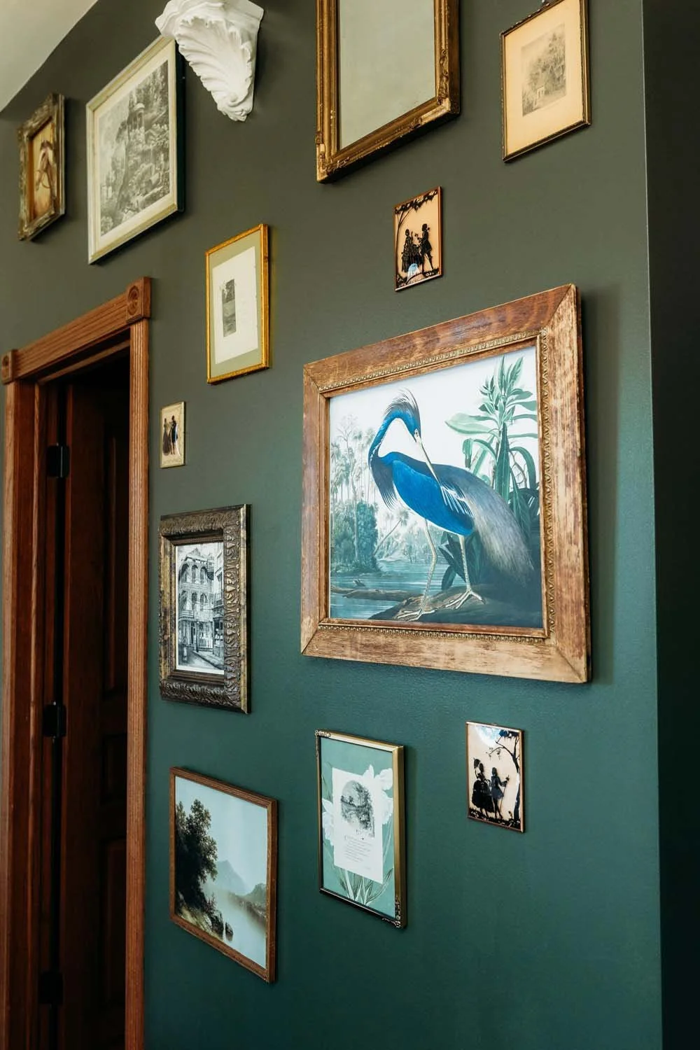 Green wall decorated with various framed artwork and photographs, including a large painting of a heron.