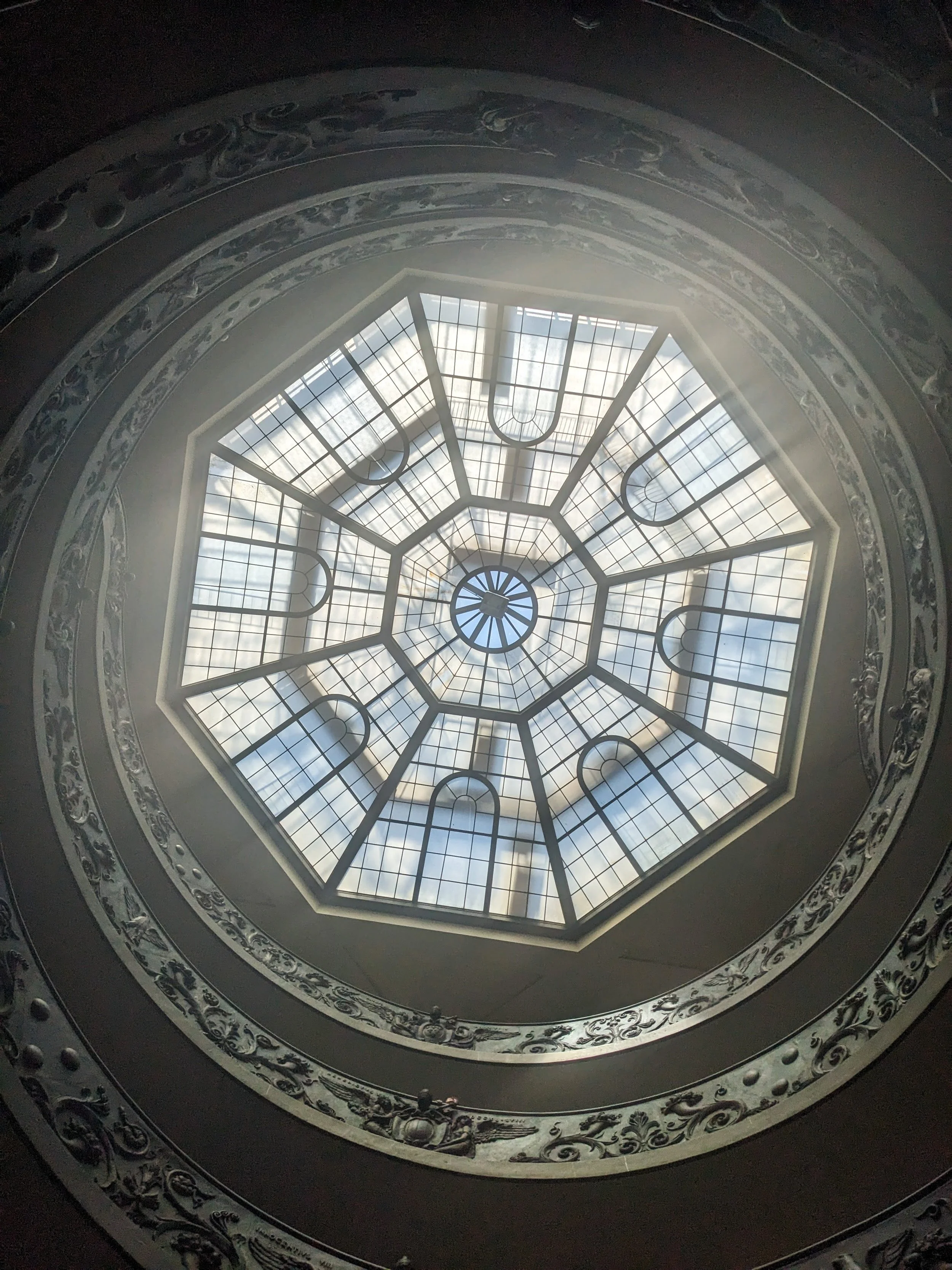 View from the ground floor of a cathedral, looking up at light shining through an octagonal window.