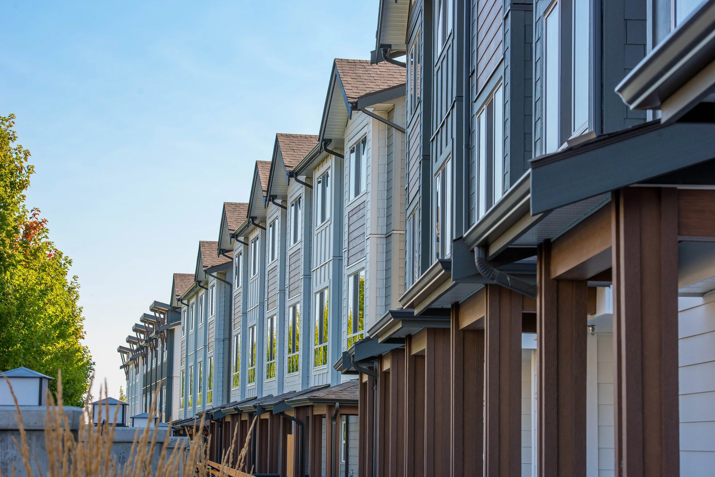 Row of modern townhouses with large windows, wooden and siding exteriors, under a clear blue sky.