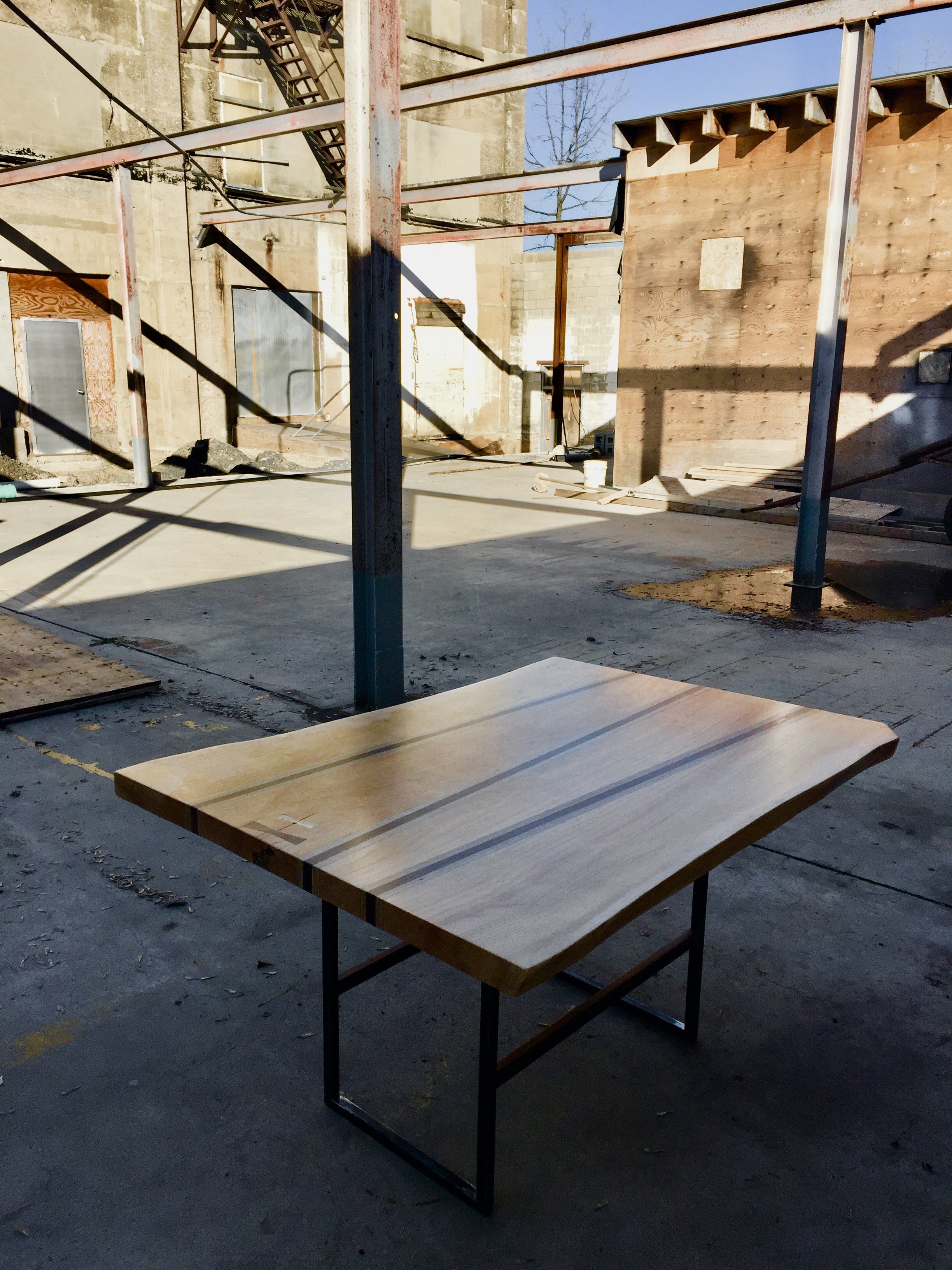 A wooden table with black metal legs in an unfinished construction site with scaffolding and building materials.