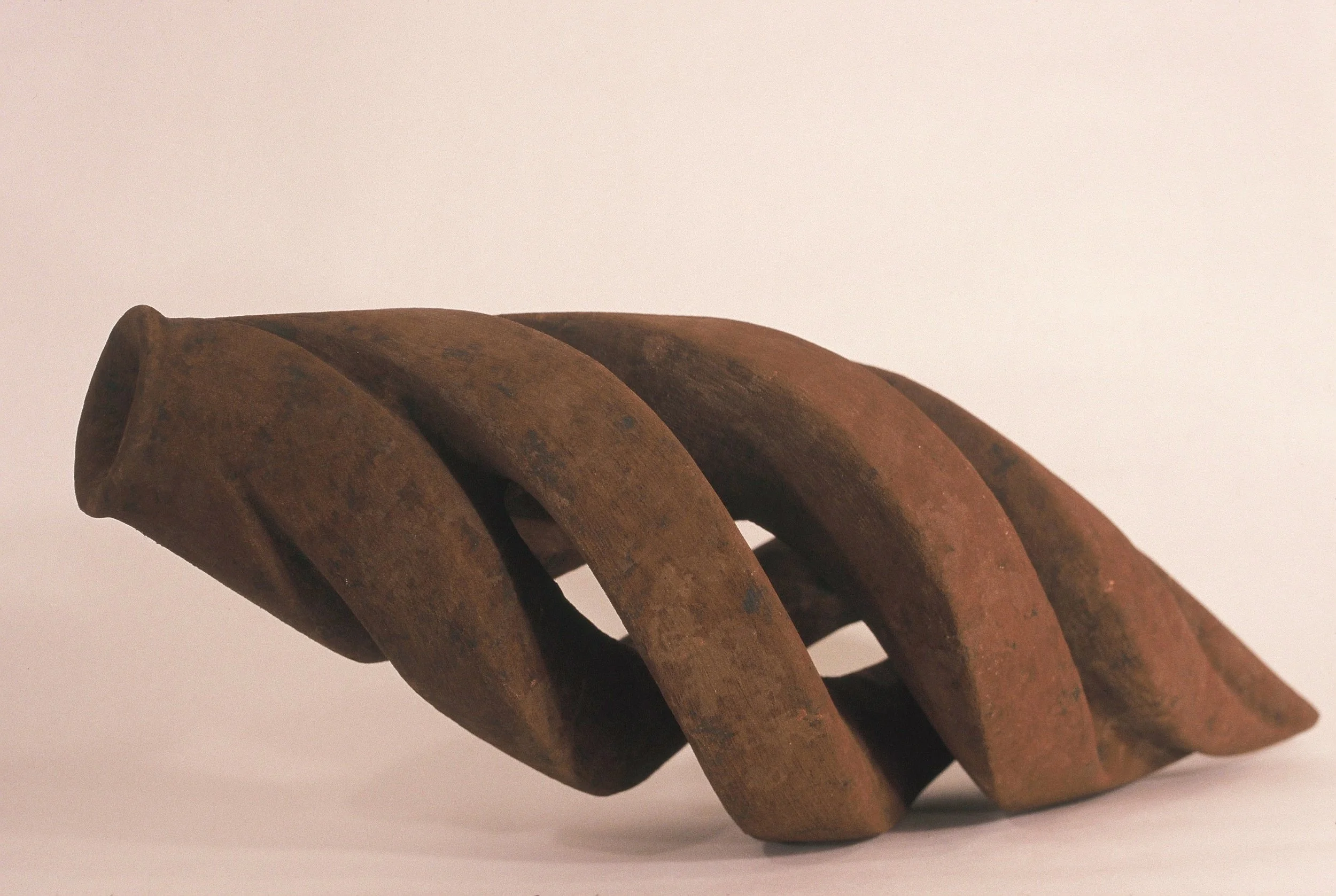 A twisted, rusted metal sculpture with an abstract, spiral shape against a plain, light background.