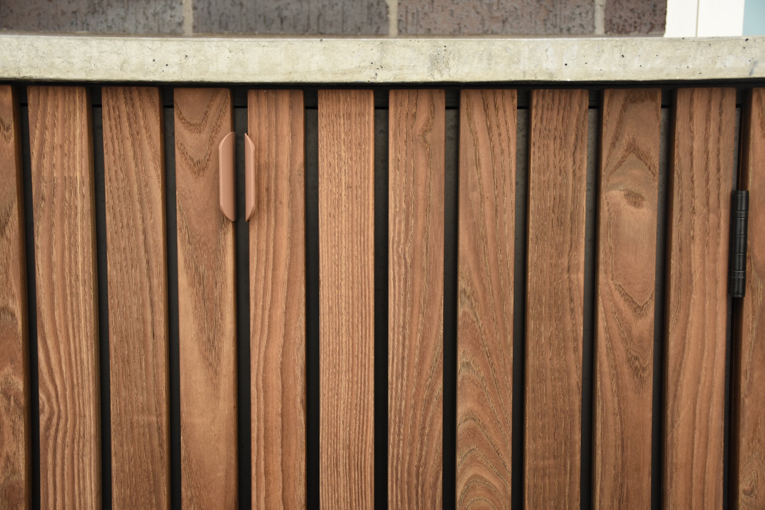 Close-up of a wooden cabinet door with vertical wood planks, a beige handle, and a black hinge on the right side.