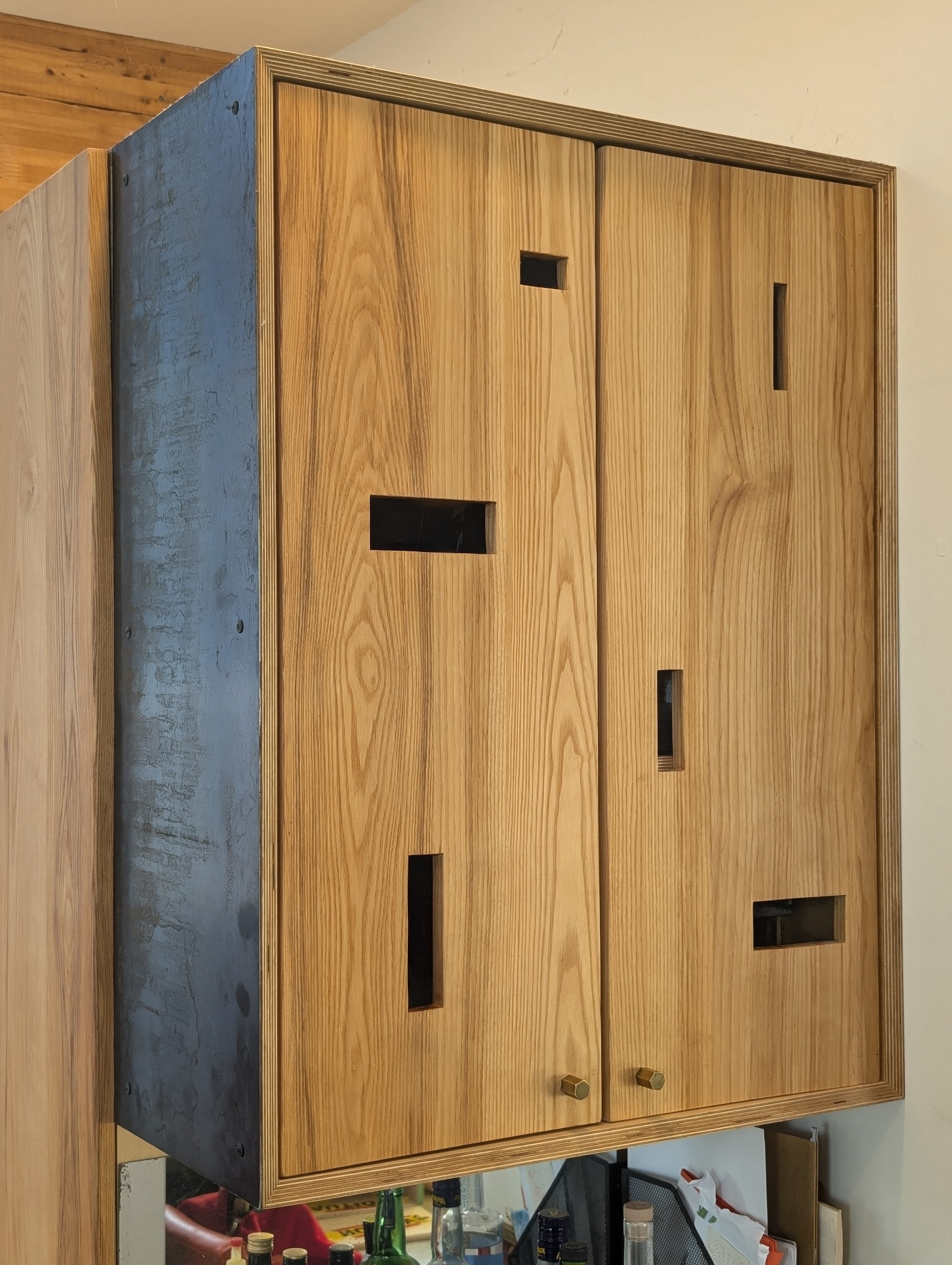 A wooden cabinet with a metal side panel, featuring multiple rectangular cut-outs and two small brass knobs at the bottom.