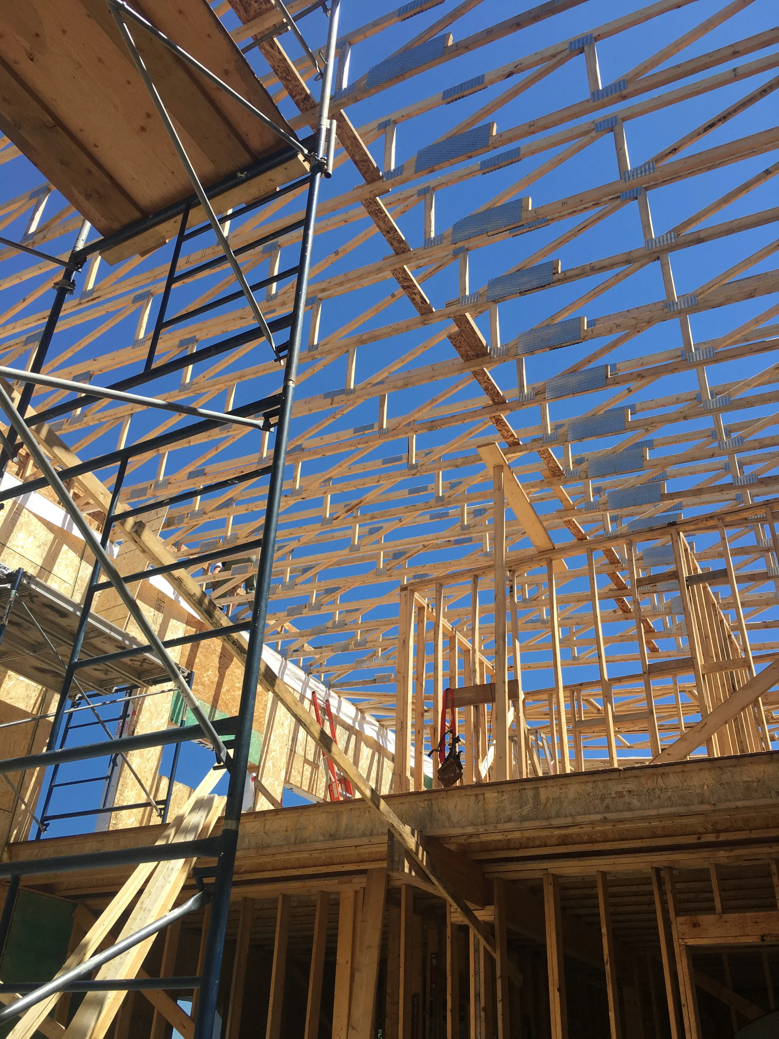 Wooden framing of a building under construction with scaffolding and blue sky in the background.