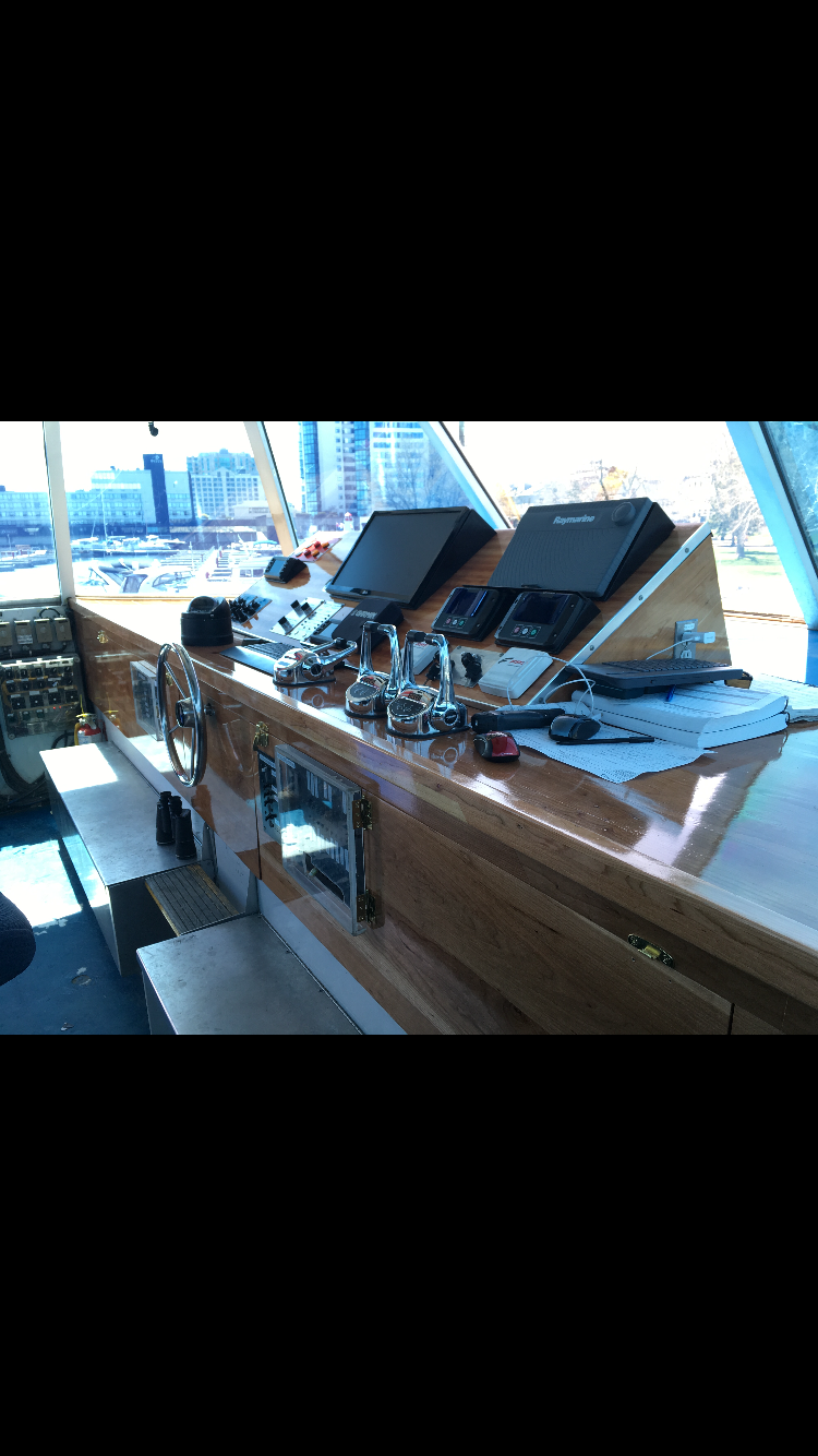Boat bridge or control station with navigational equipment, padlocks, and a view of a city skyline through windows.