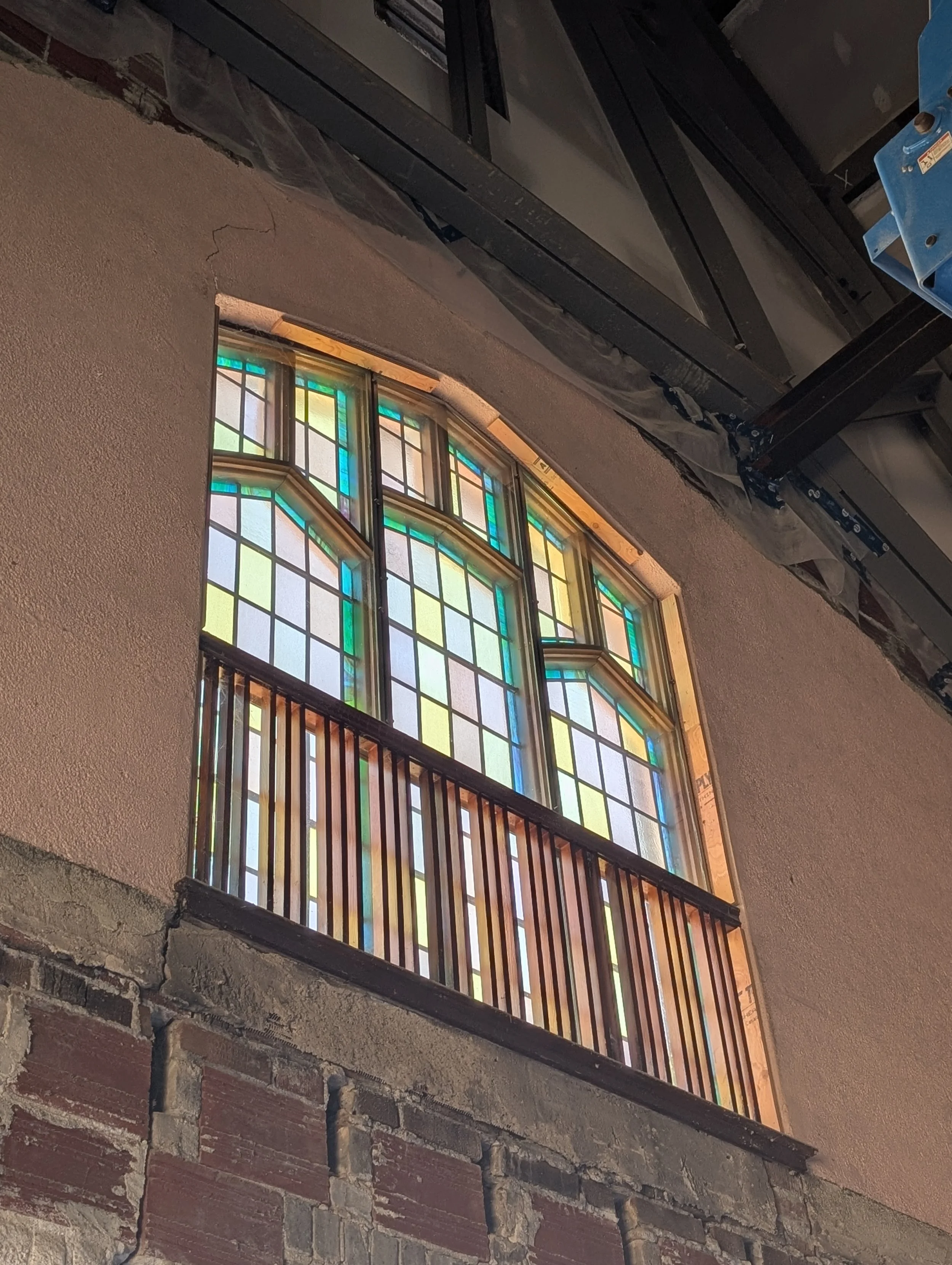 A stained glass window with colorful geometric patterns, installed in a wall with exposed bricks and plaster, amidst construction or renovation work.