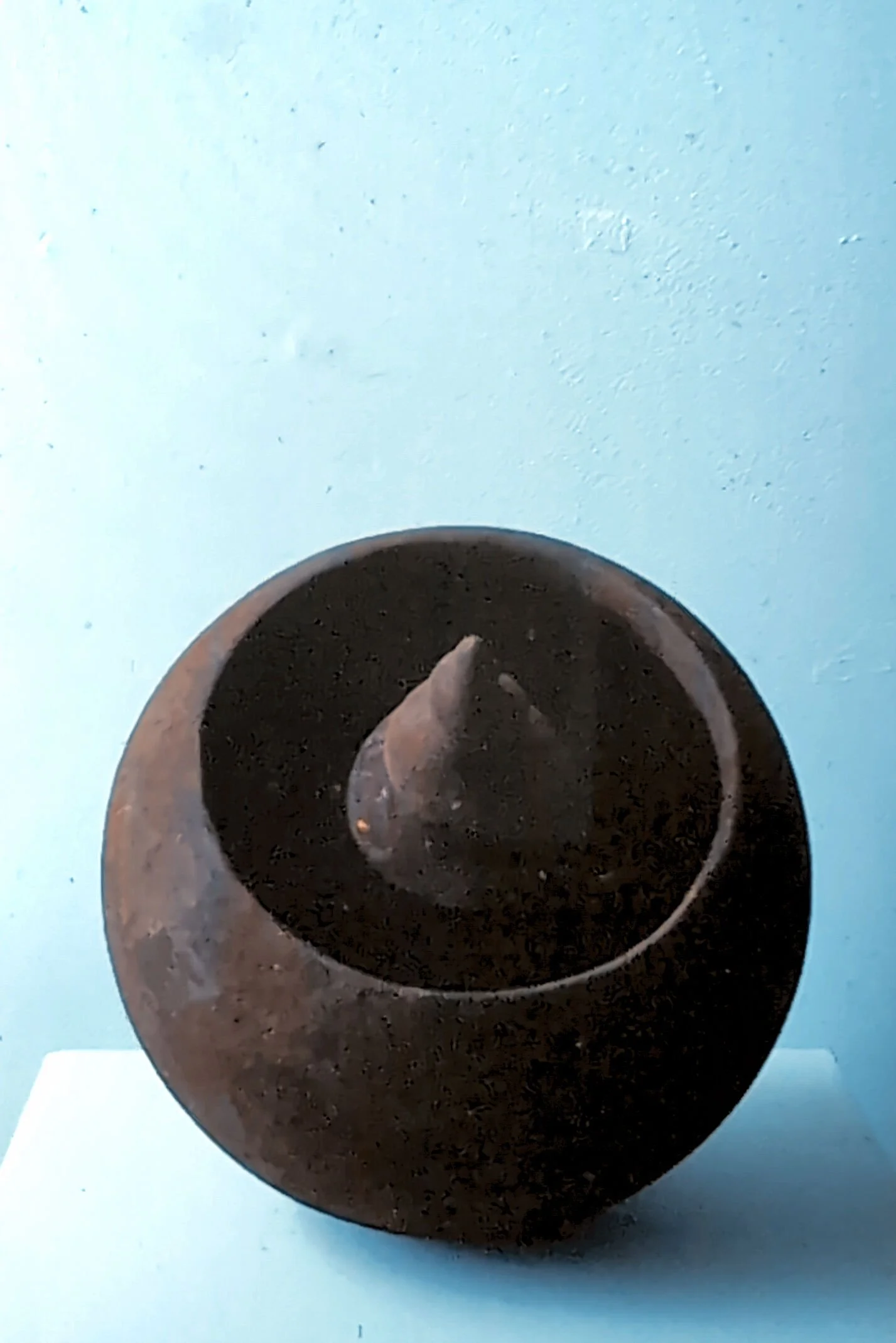 A small animal sculpture, possibly a bird, inside a round, hollow, rust-colored vessel with an opening at the top.