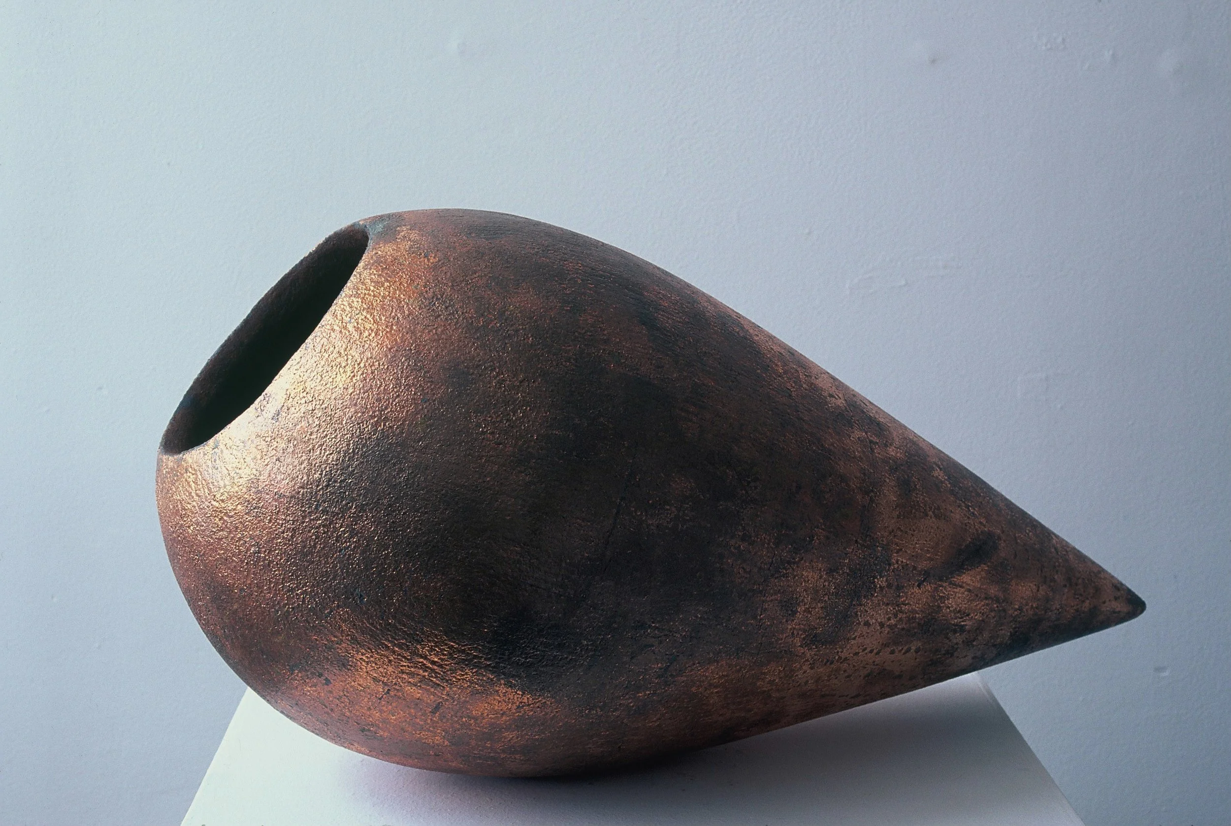 A large, dark, textured, teardrop-shaped ceramic vessel with a wide opening at the top, displayed on a white surface against a plain light background.