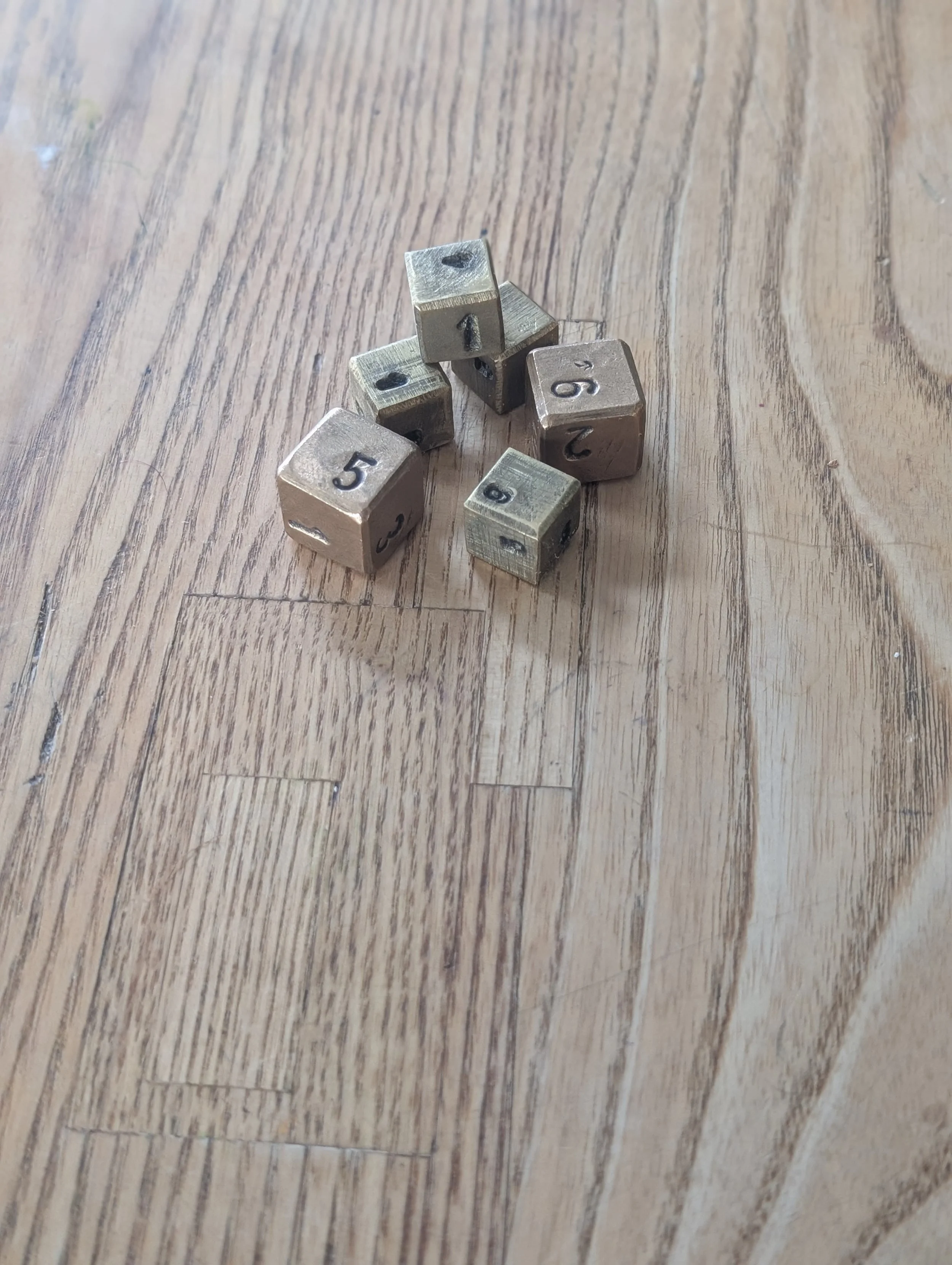 Six metal dice with numbers from 1 to 6, arranged on a wooden floor.