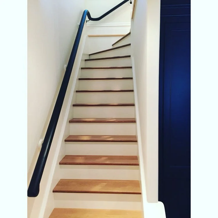 Custom designed and integrated wooden staircase with dark handrail on the left and a blue wall on the right, leading upward.