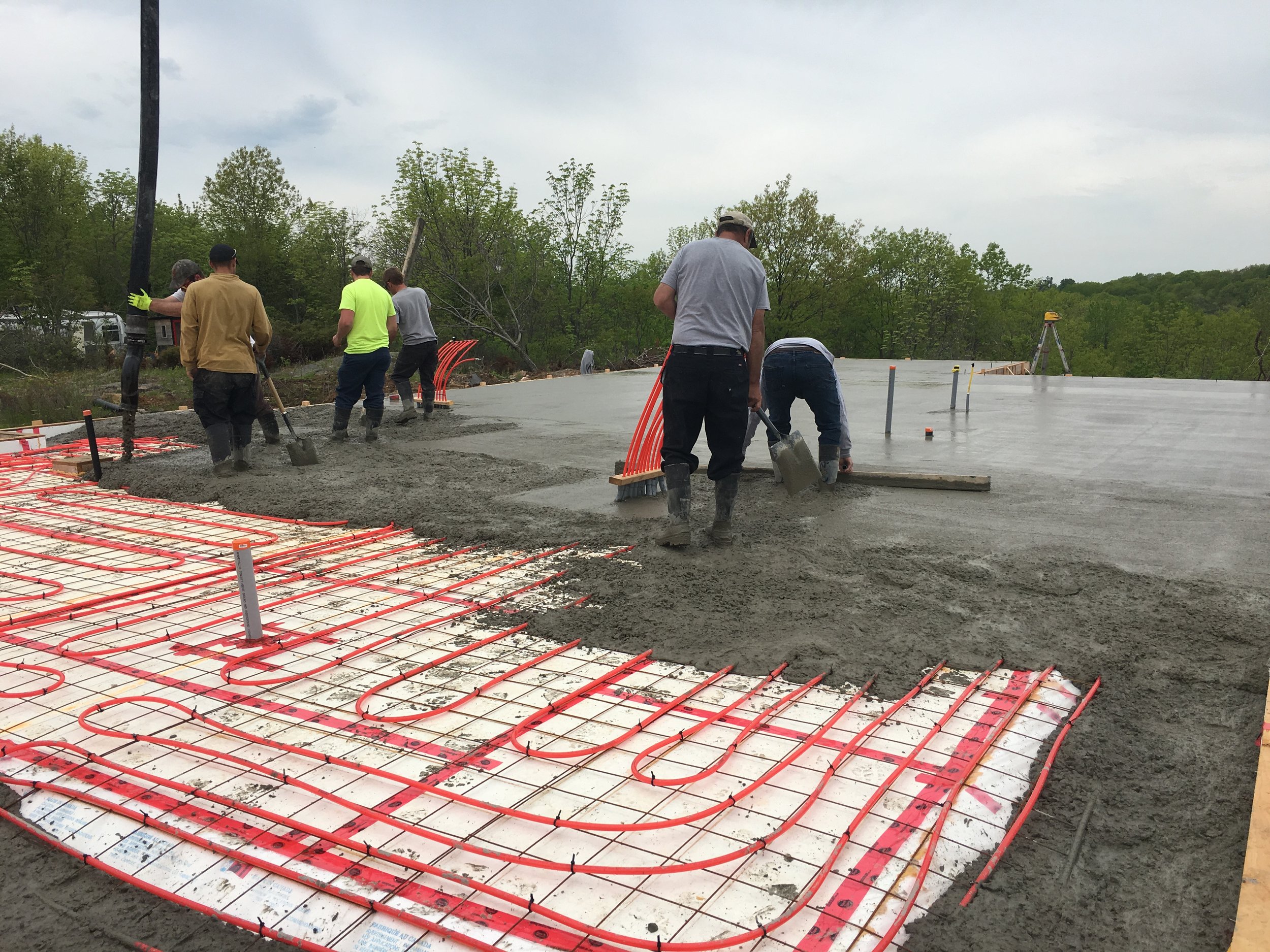 Workers pouring concrete for a building foundation with radiant heating pipes installed.