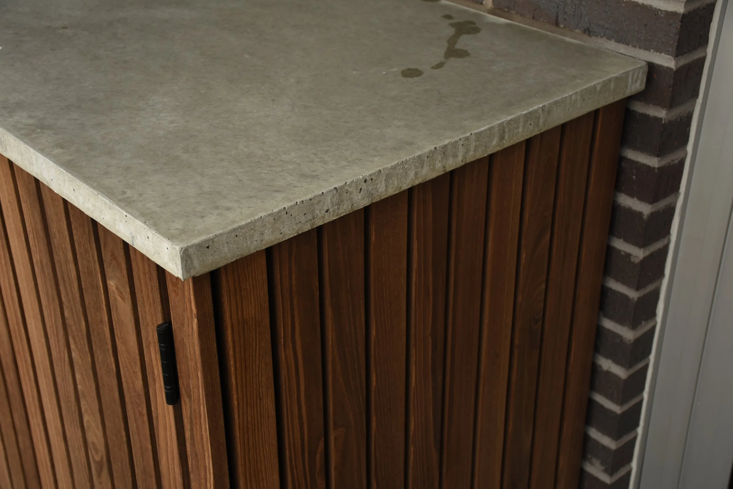 Concrete countertop with a water stain on a wooden cabinet next to a brick wall.