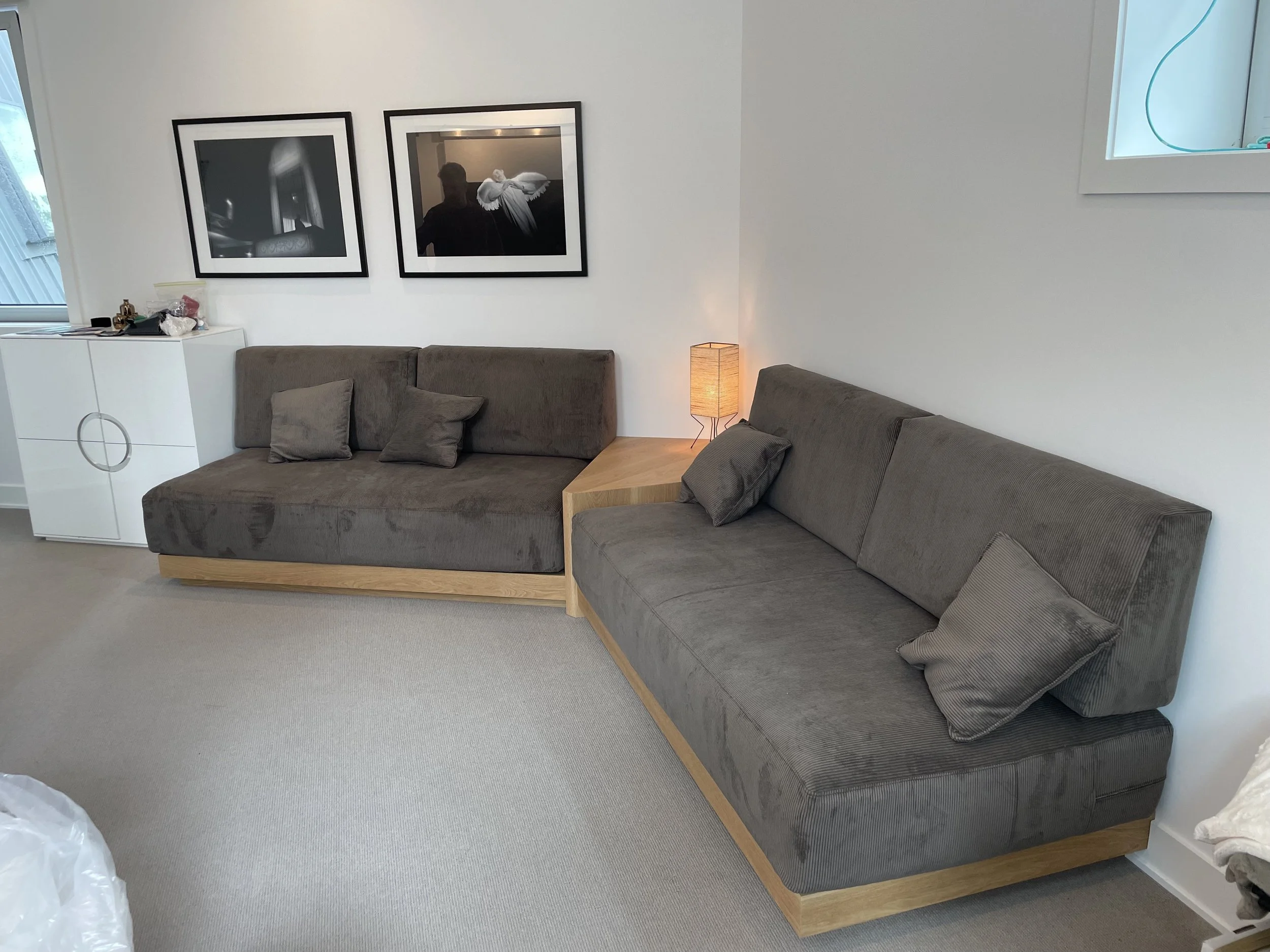 Living room with two gray sofas, two throw pillows on each, a side table with a lamp, and wall art including black-and-white framed photographs.
