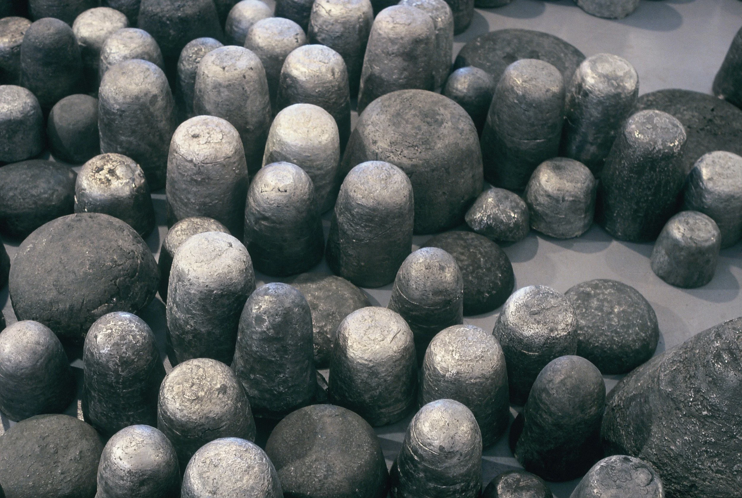 Multiple metallic or stone objects that resemble bullets or cannonballs arranged on a flat surface.