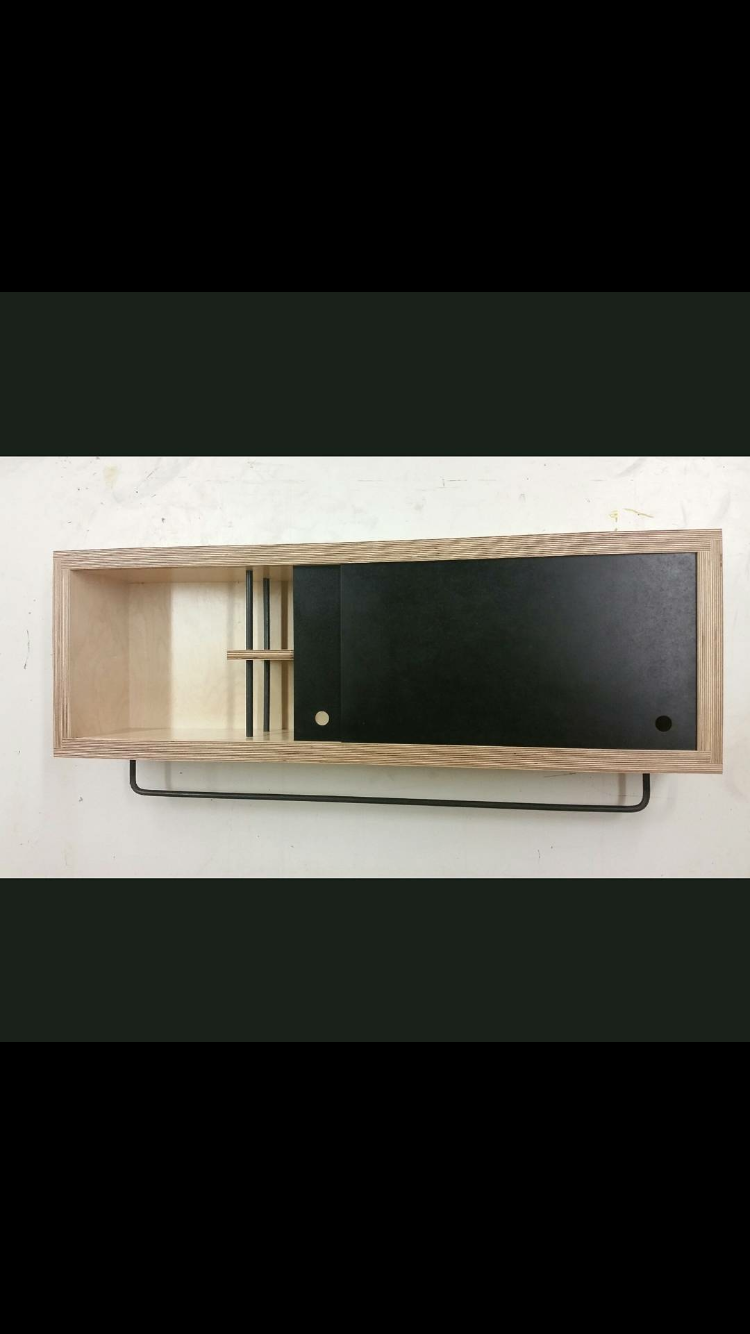Wall-mounted wooden storage unit with black sliding door and circular cut-outs, resting on a black metal frame.