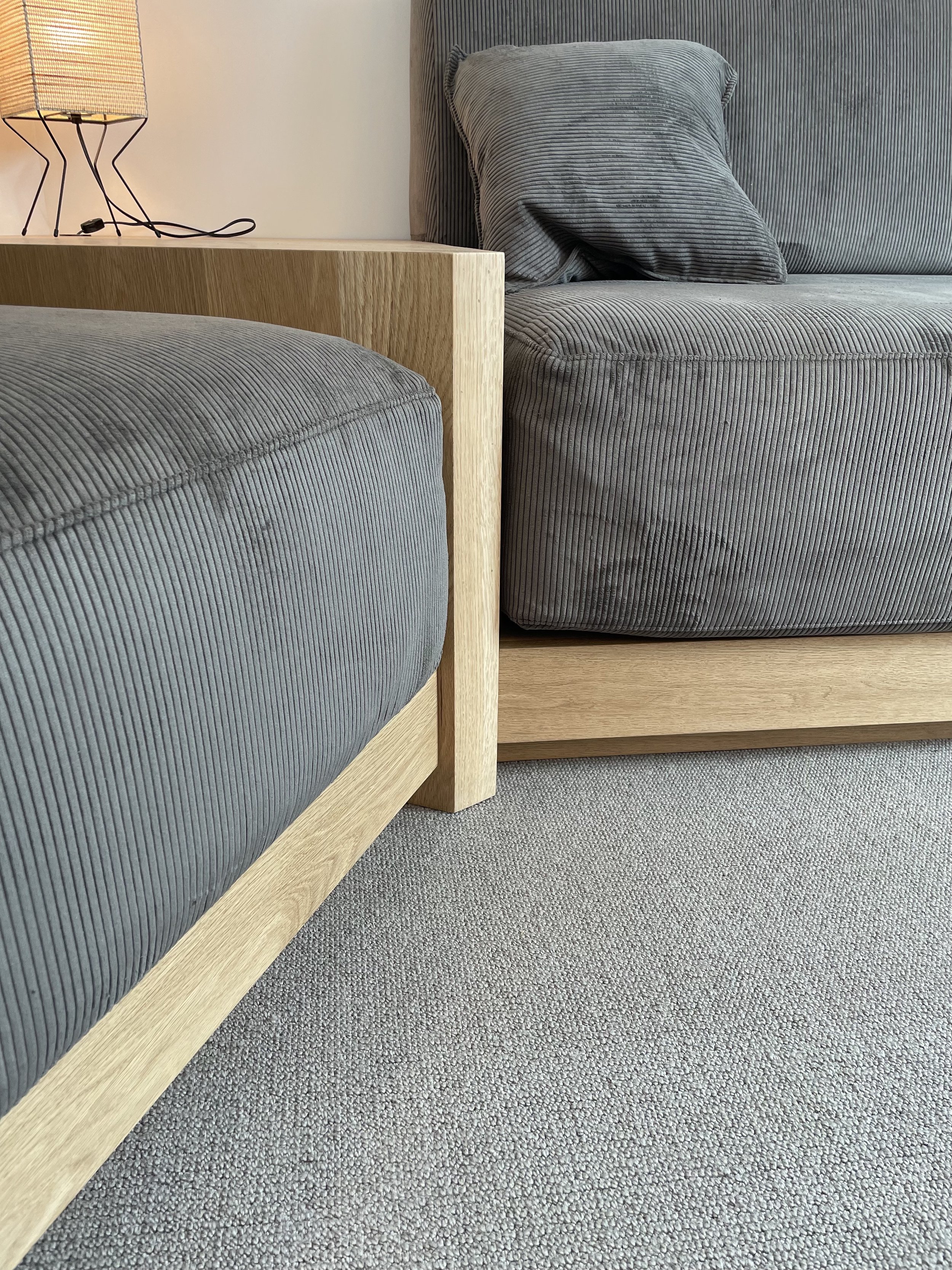 Close-up of a modern bedroom with two gray corduroy sofas, wooden side table, and a small lamp on top.