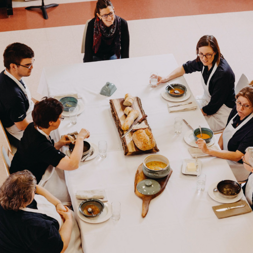 People gathered around a dining table with bread and soup, enjoying a meal together.