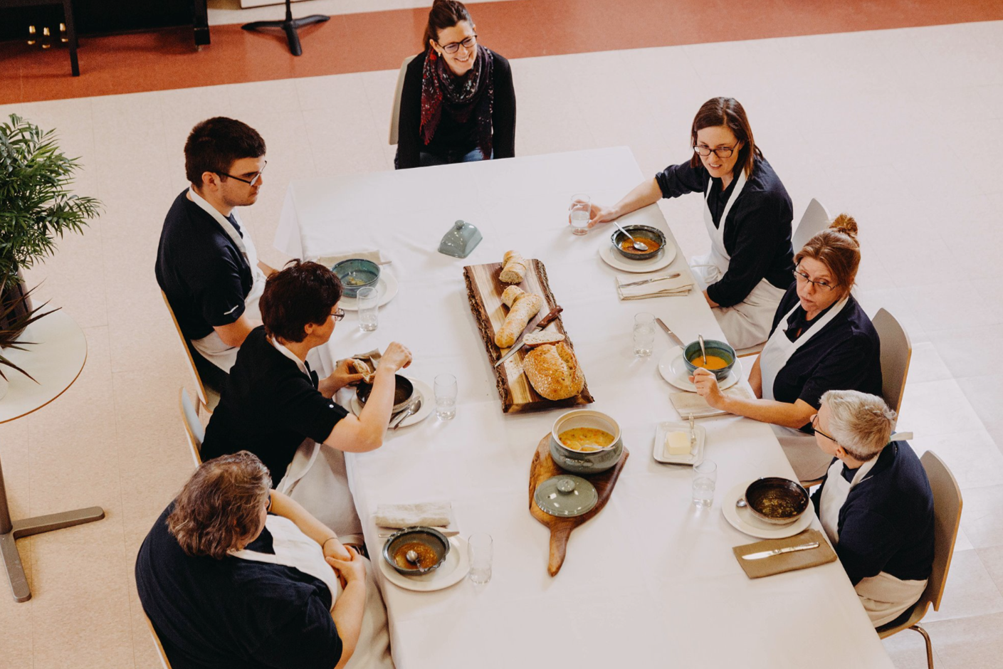 People sitting around a banquet table with bread, soup, and water, engaged in a meal and conversation.