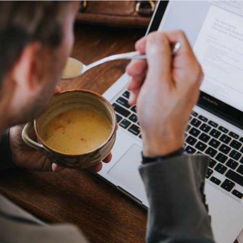Person eating soup with a spoon while working on a laptop.