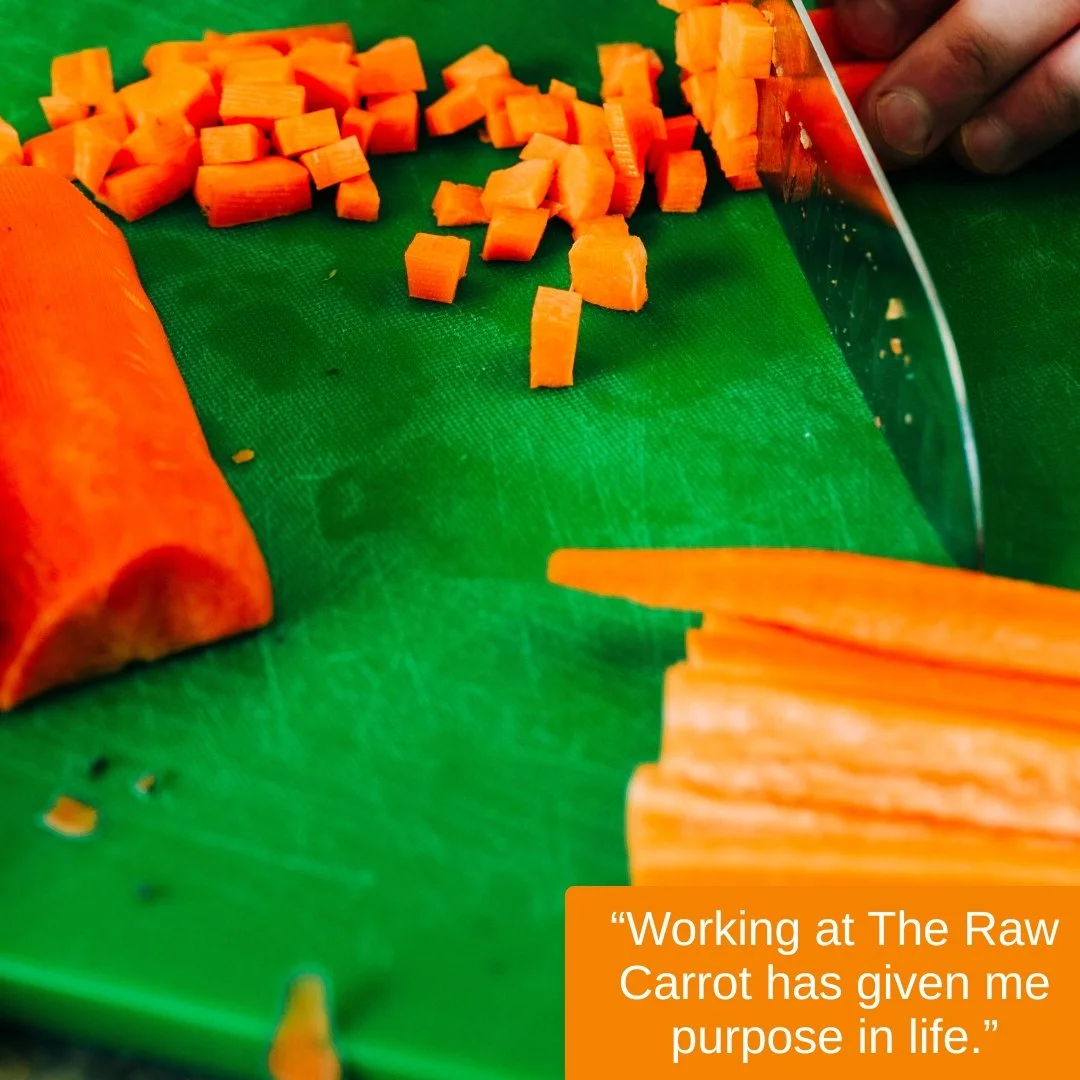 Chopped raw carrots on a green cutting board with a partially sliced carrot and a person chopping in the background.