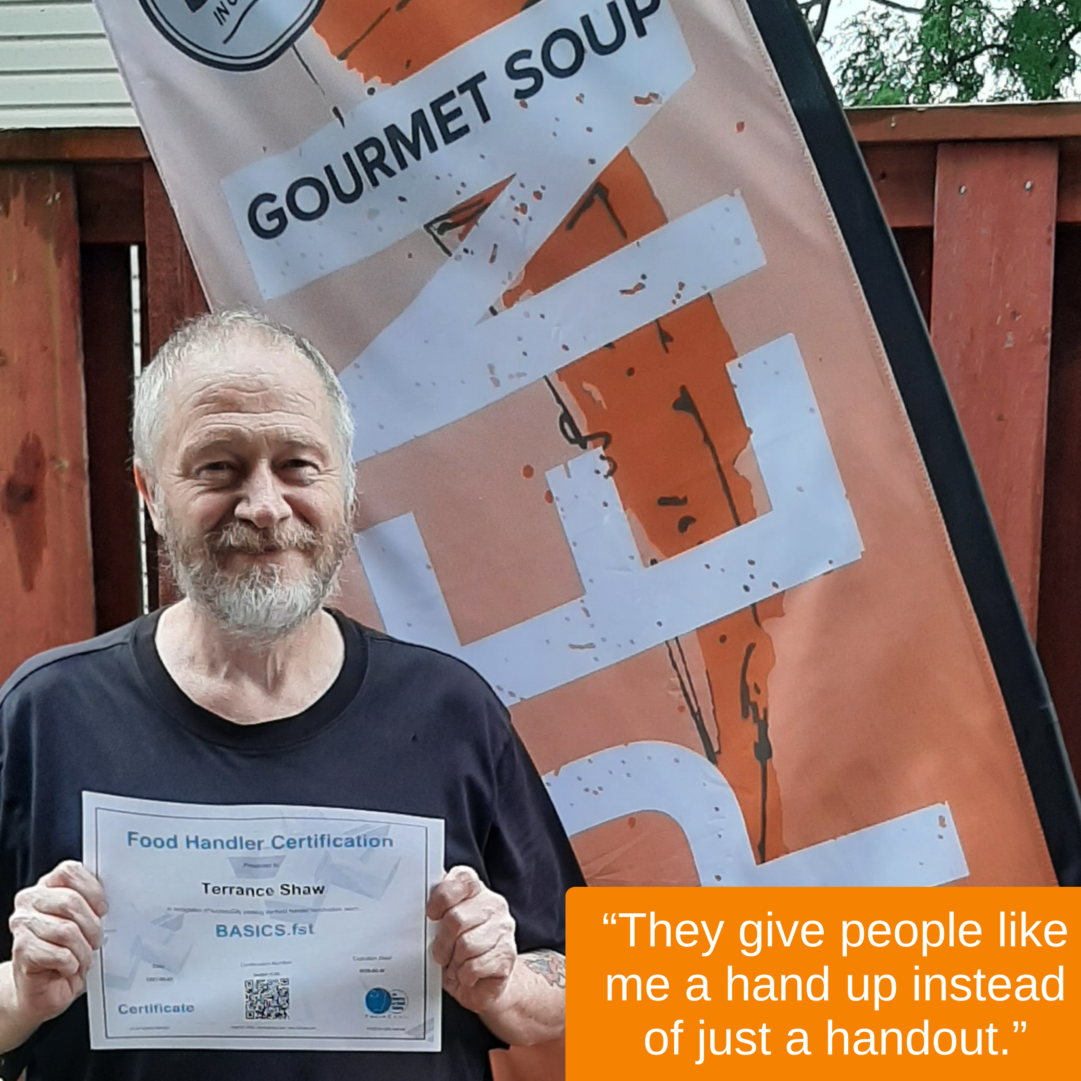 A man with a beard and short gray hair holding a Food Handler Certification certificate, standing outside near a wooden fence and a large banner with ‘Gourmet Soup’ written on it. An orange box with white text reads, ‘They give people like me a hand up instead of just a handout.’
